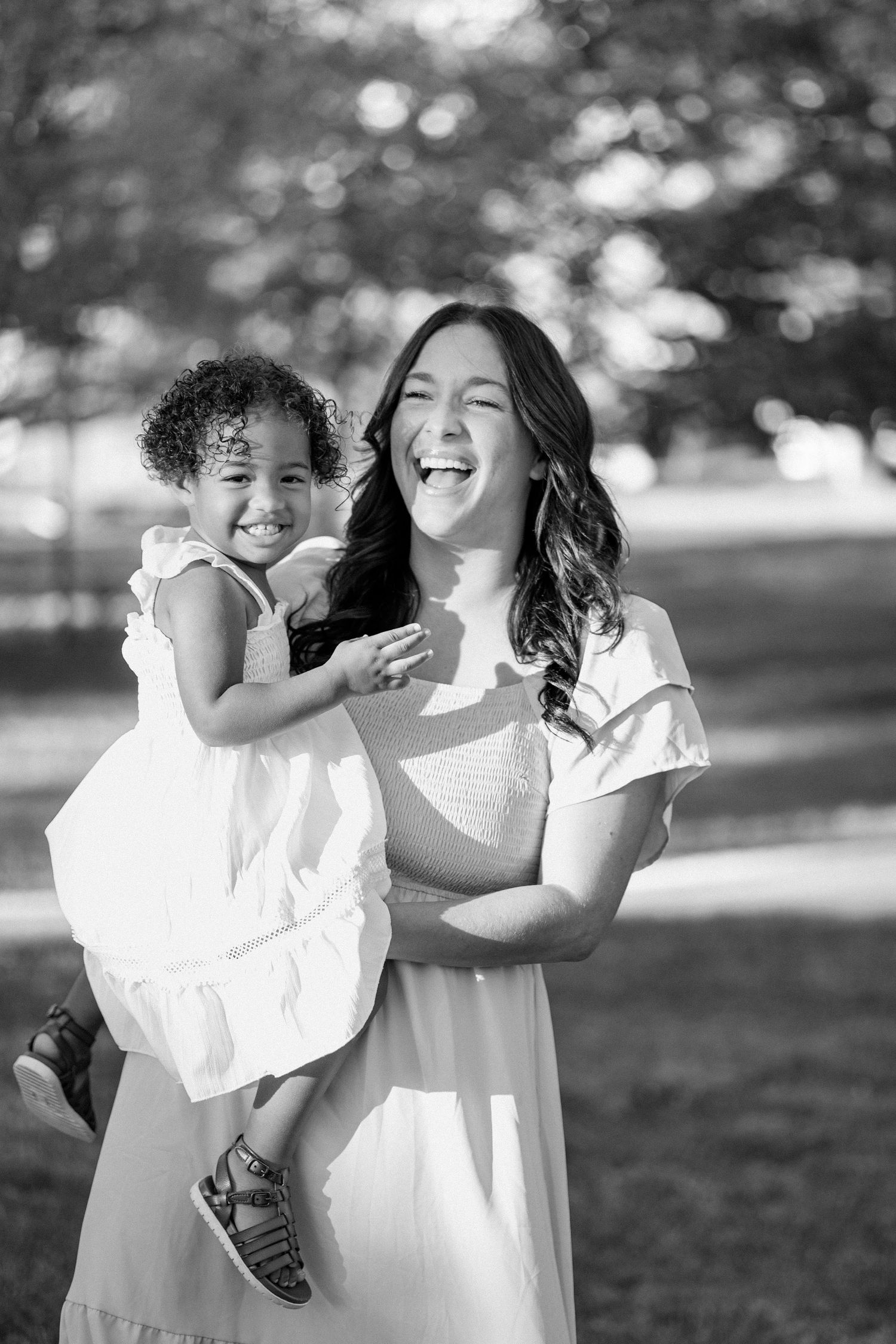 Black and white photo of mother and daughter laughing together in park.