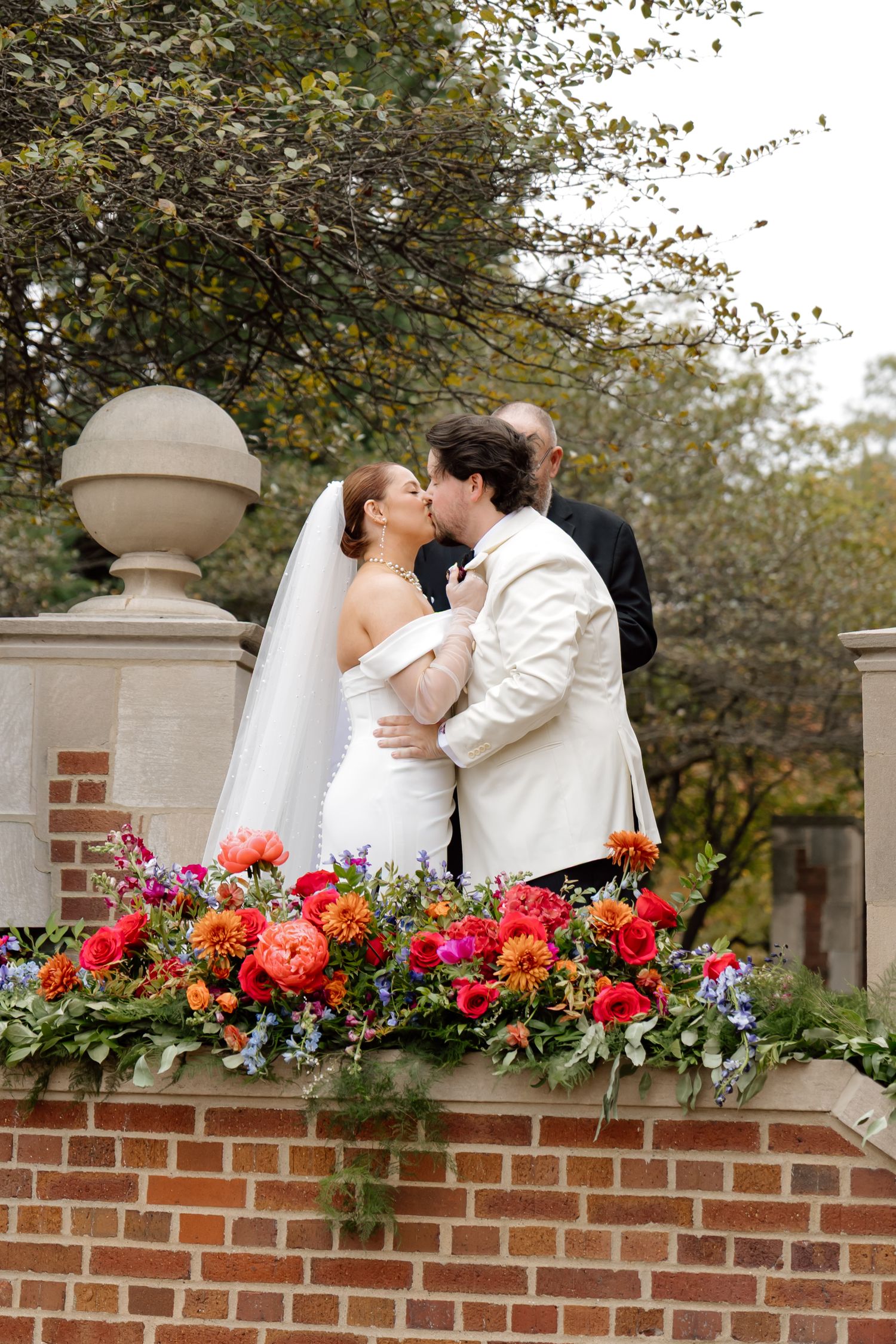 Bride and groom sharing first kiss at outdoor ceremony above colorful floral arrangement.