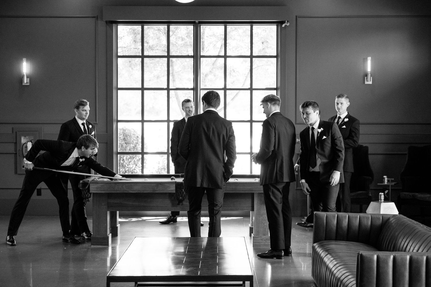 Groomsmen in suits around a pool table in elegant black and white wedding photo at The Monroe wedding venue in West Des Moines, Iowa.