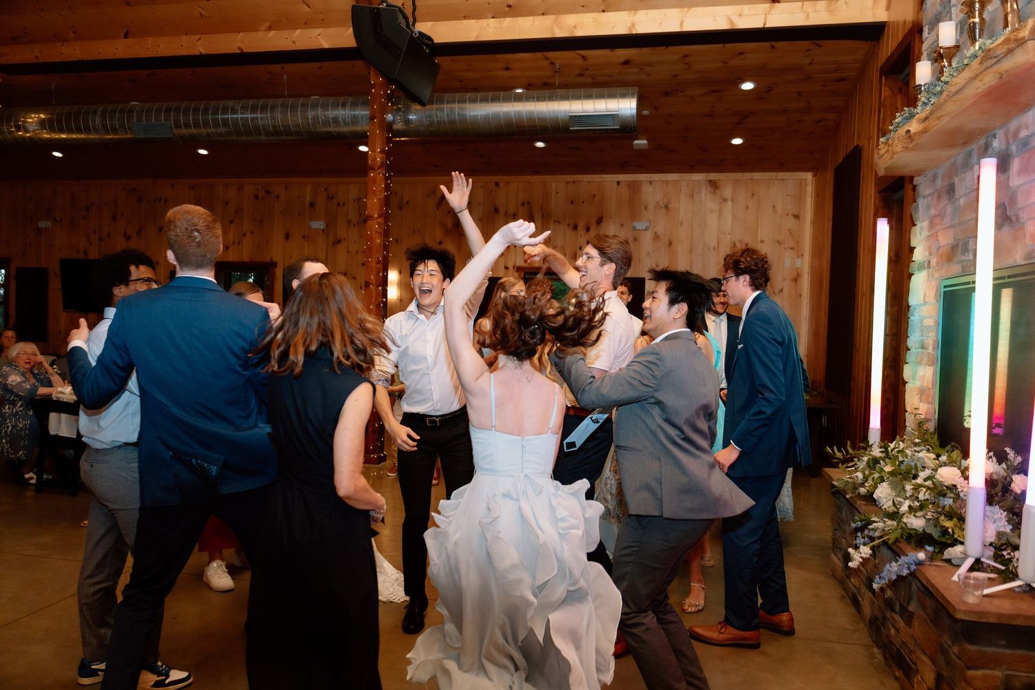 A joyful bride in a white dress dances with wedding guests on the reception dance floor.
