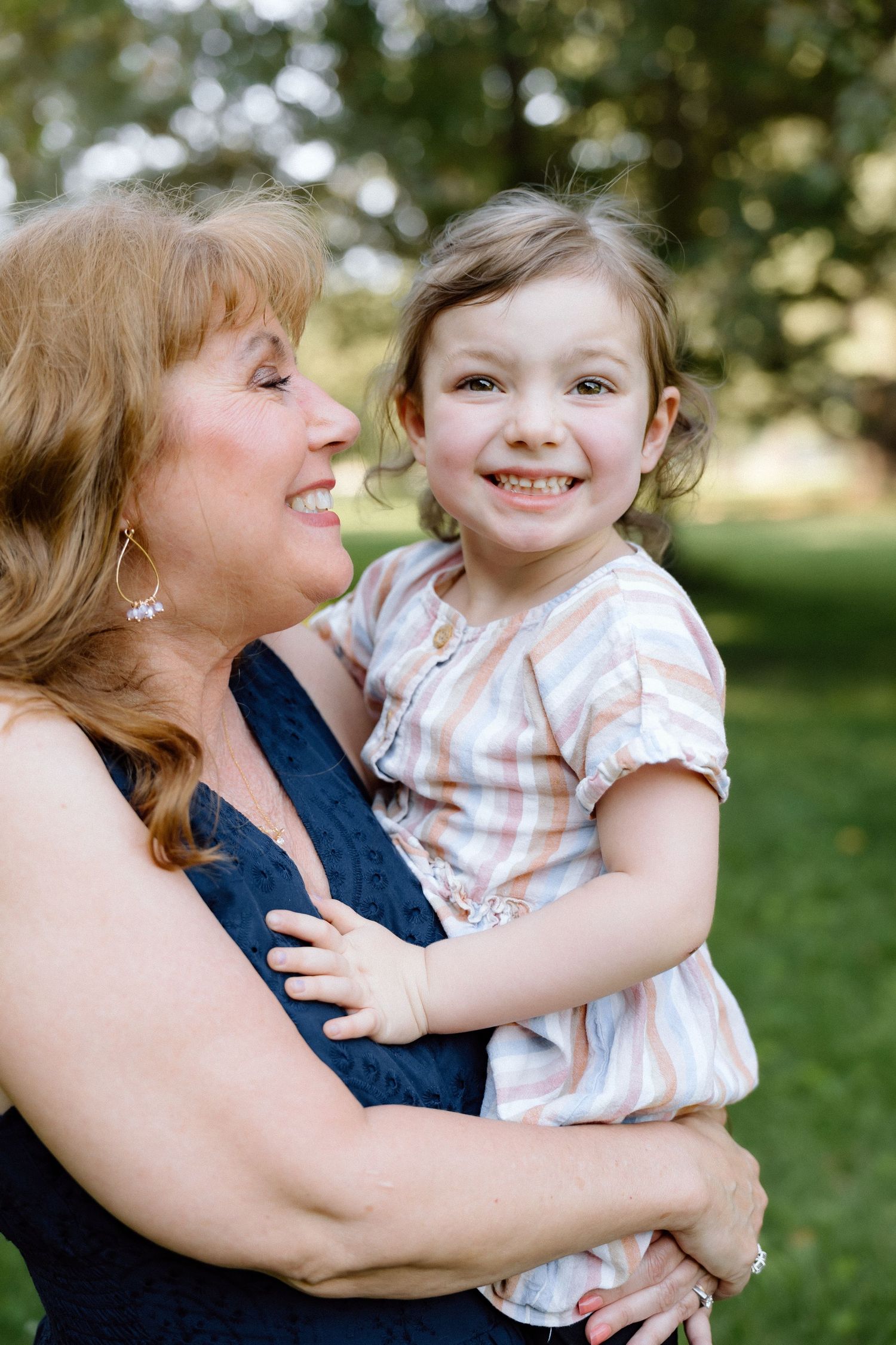 Grandmother smiling and holding a happy toddler girl outdoors in a green park setting.