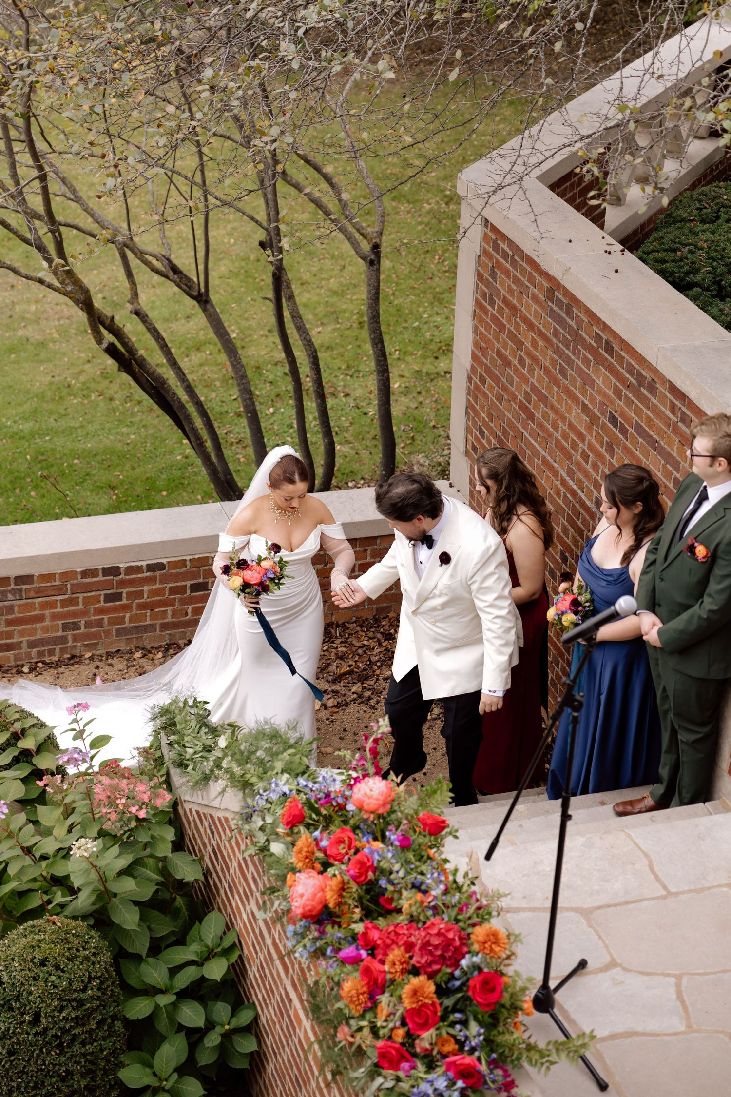 Aerial view of bride and groom holding hands at outdoor wedding ceremony with colorful florals.