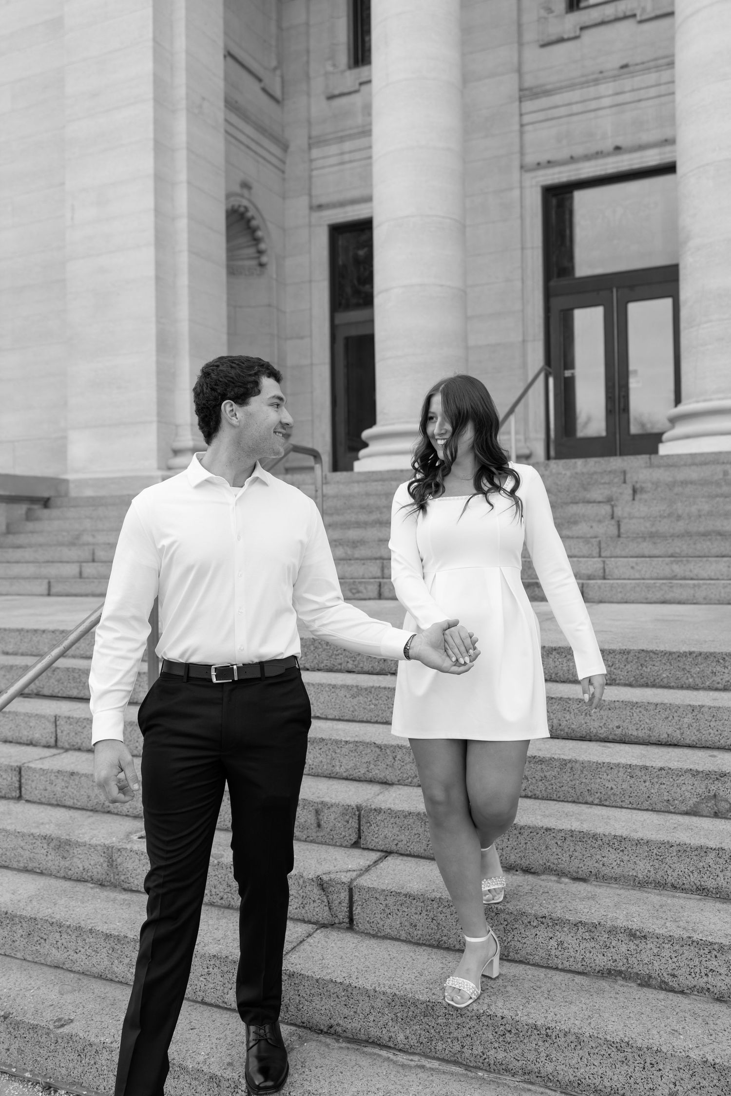 Black and white photo of couple holding hands walking down grand stone steps.