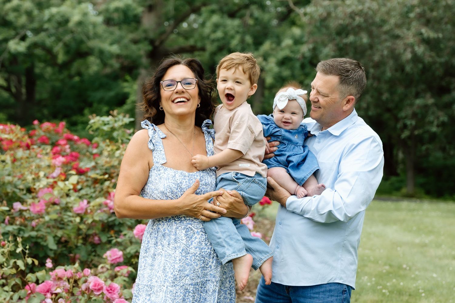 Joyful family of four laughing together among blooming roses in a green garden.