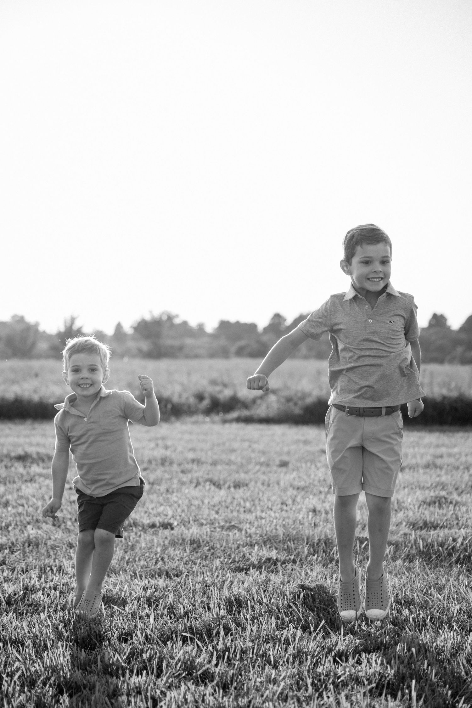 Black and white photo of two young boys running and jumping joyfully in an open grassy field.