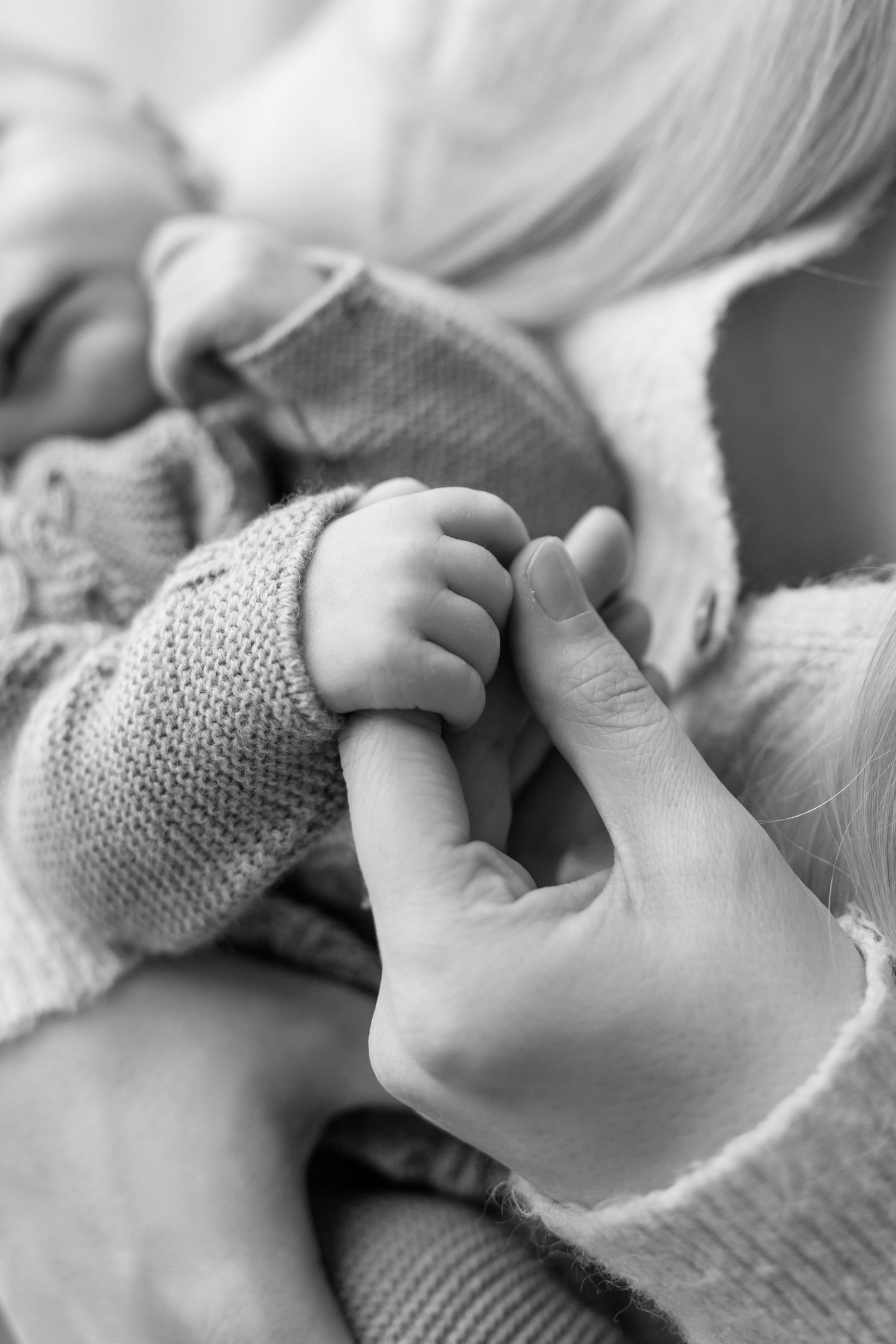 Black and white close-up of a newborn baby grasping an adult's finger in a tender moment.