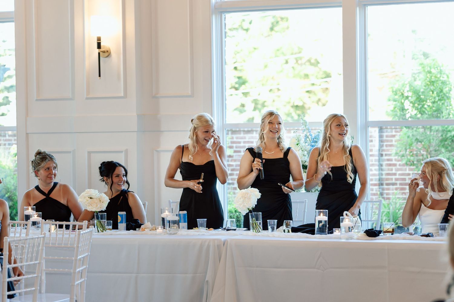 Bridesmaids laughing and giving toasts at elegant white wedding reception table at The Monroe wedding venue in West Des Moines, Iowa.