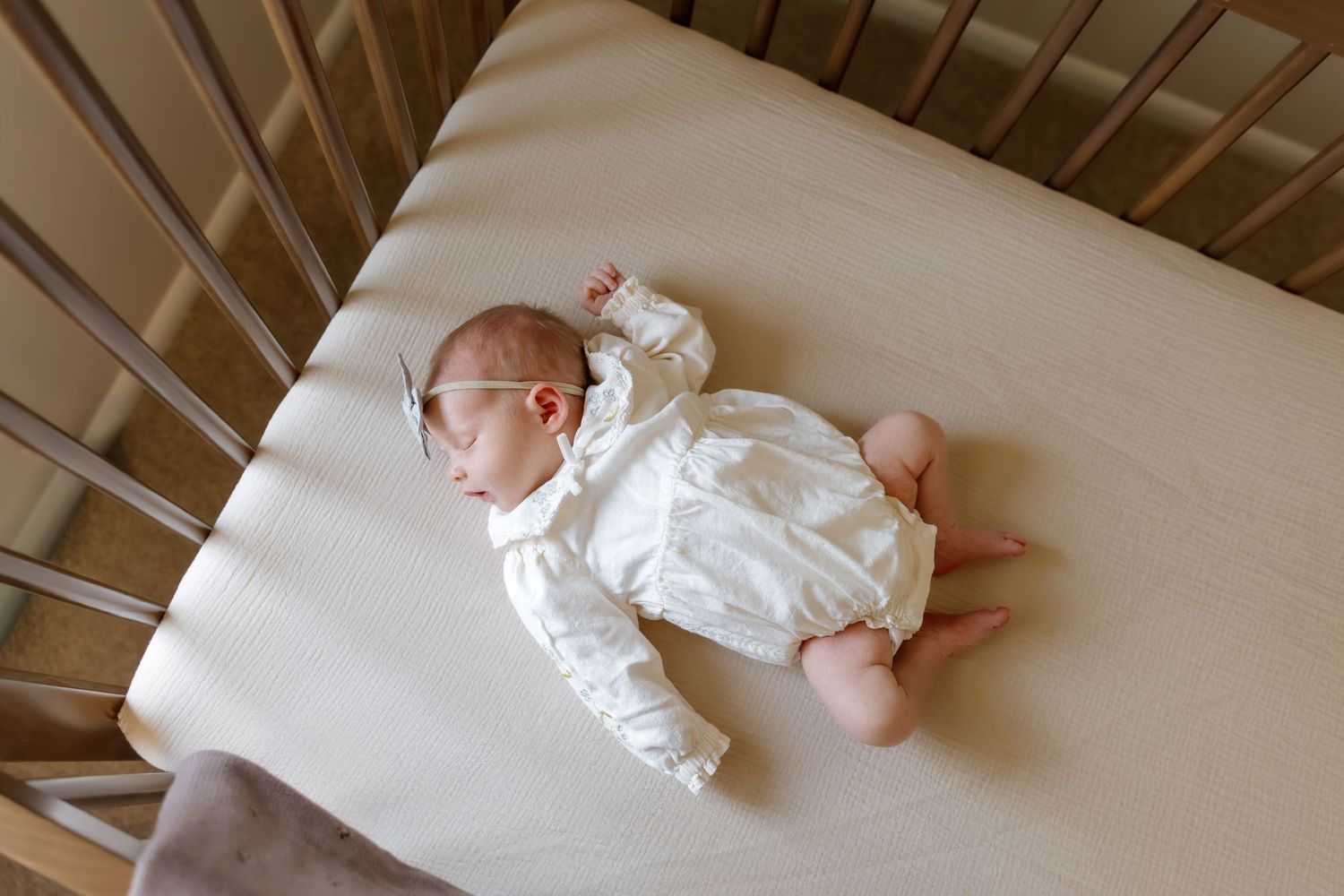 Newborn baby sleeping peacefully in a wooden crib wearing a white romper.