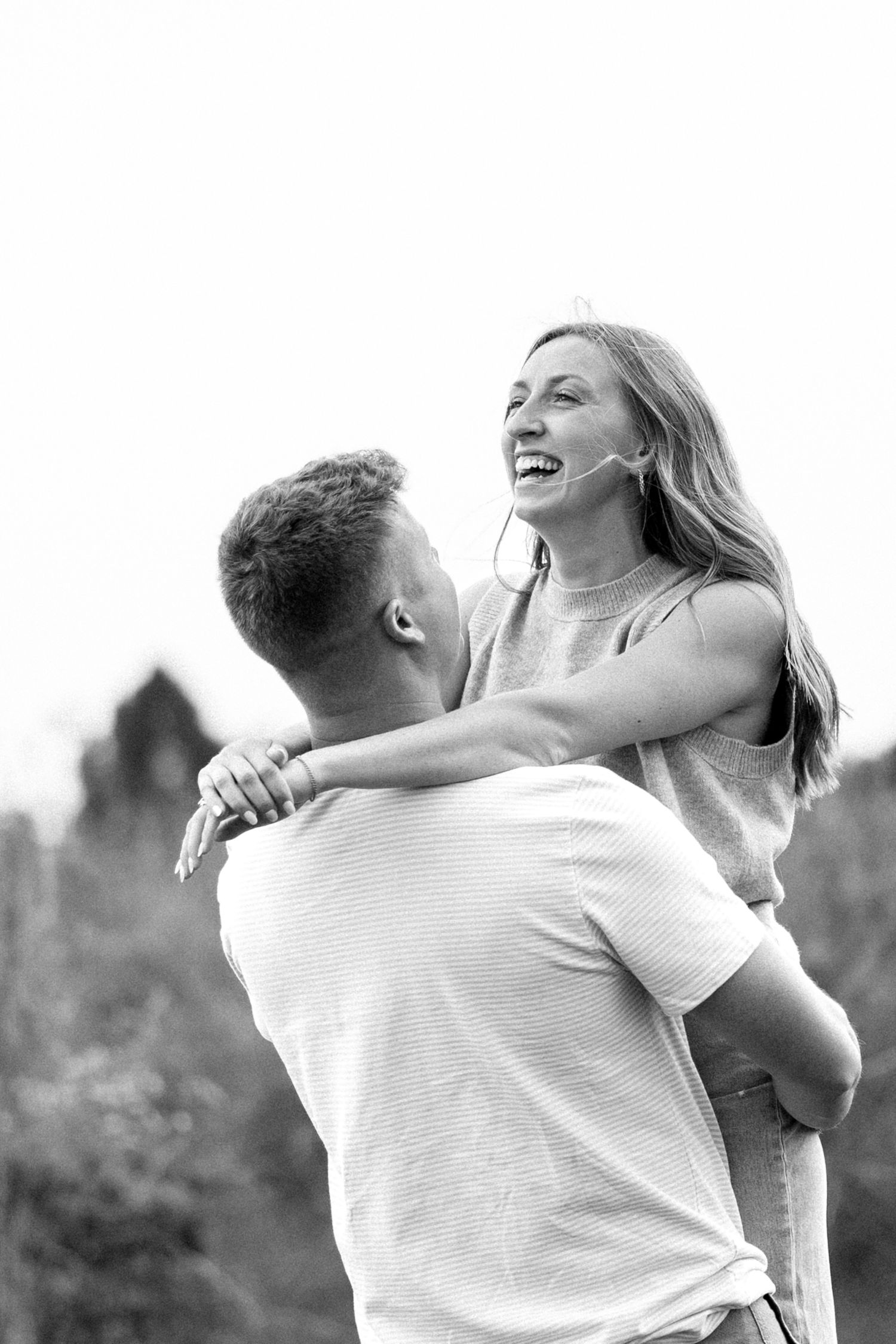Black and white photo of laughing woman being lifted by man in outdoor nature setting.