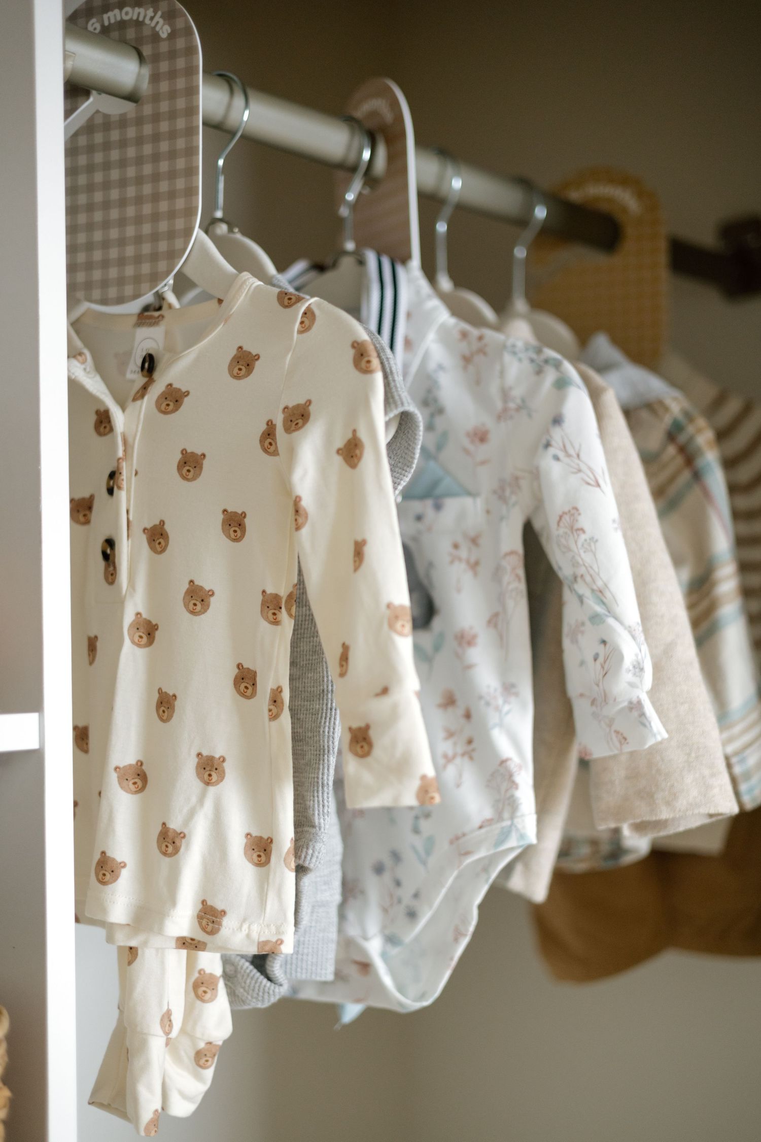 Soft neutral baby clothes with bear prints hanging on a nursery closet rod.