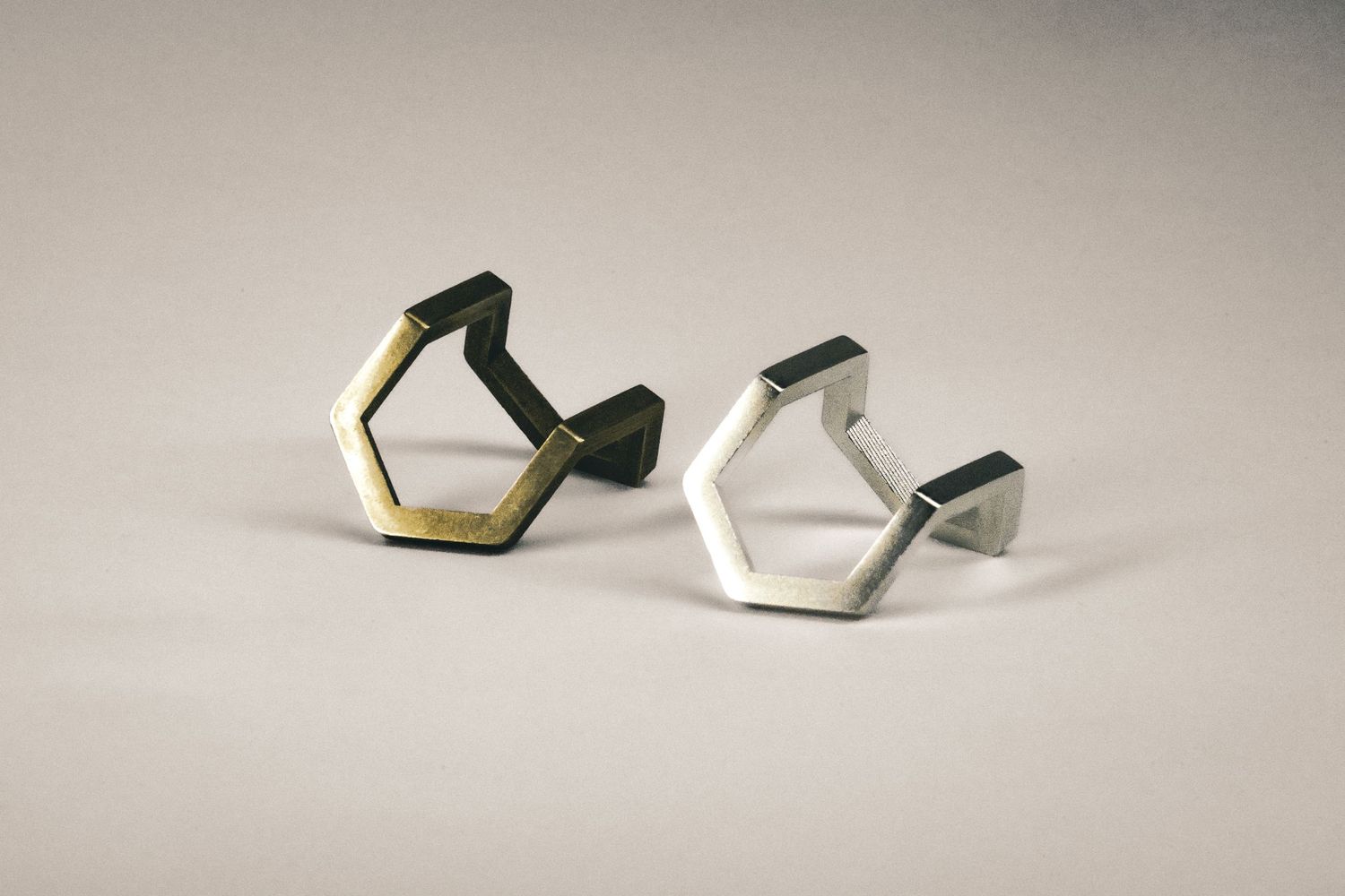 Two geometric hexagonal rings in gold and silver tones displayed on a neutral background.