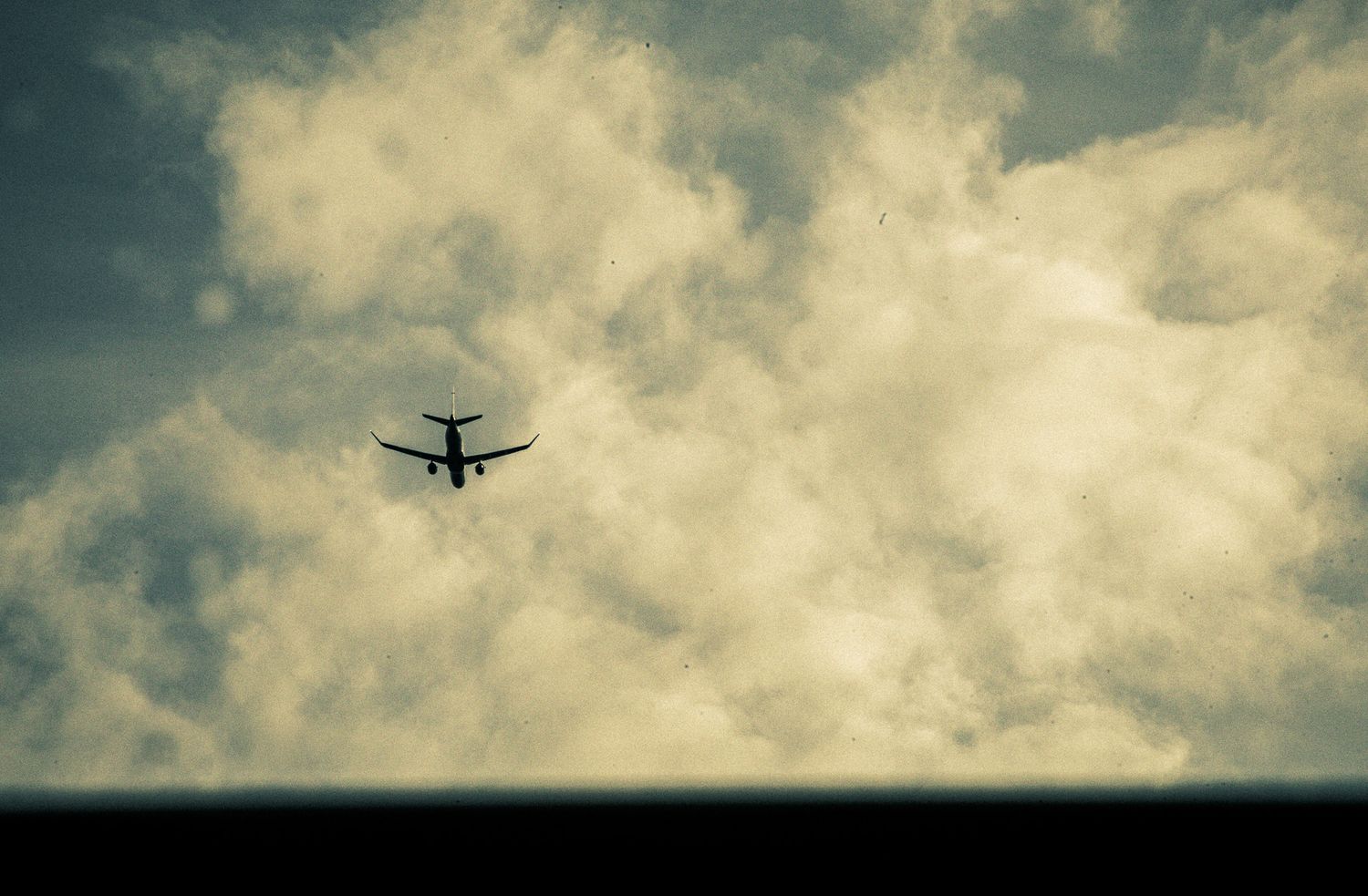 Silhouette of a commercial airplane flying through dramatic cloudy skies with golden light breaking through clouds.