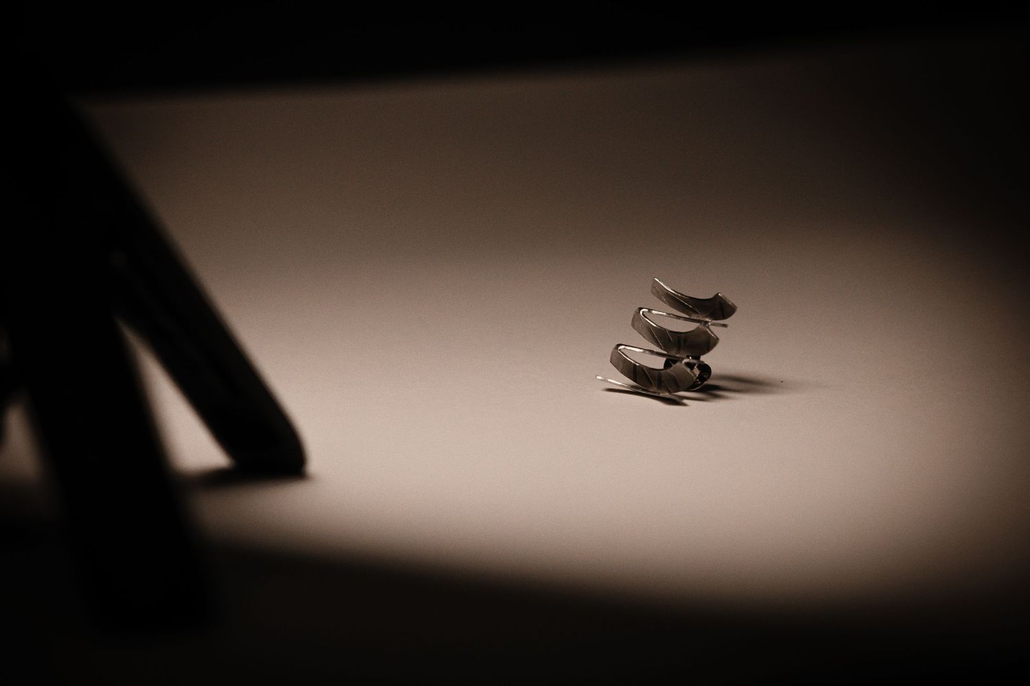 Small silver spiral earring dramatically lit against a plain surface with dark shadows in macro photography.
