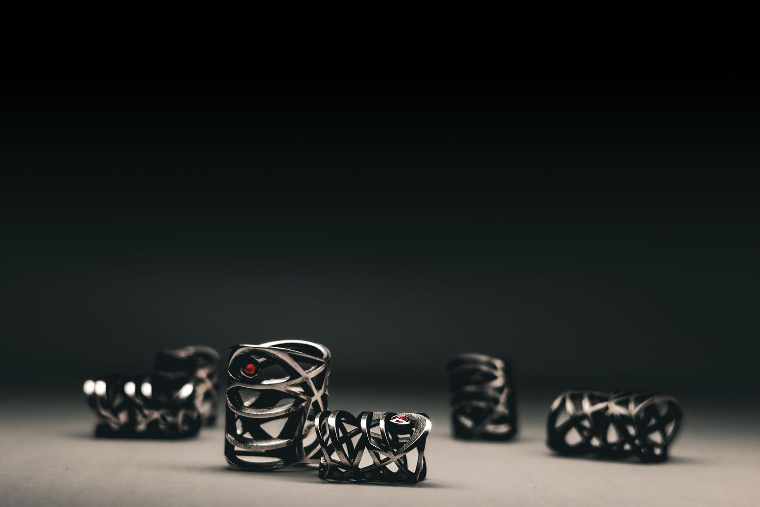 Dark metallic 3D printed geometric rings with intricate lattice patterns displayed on a neutral surface.
