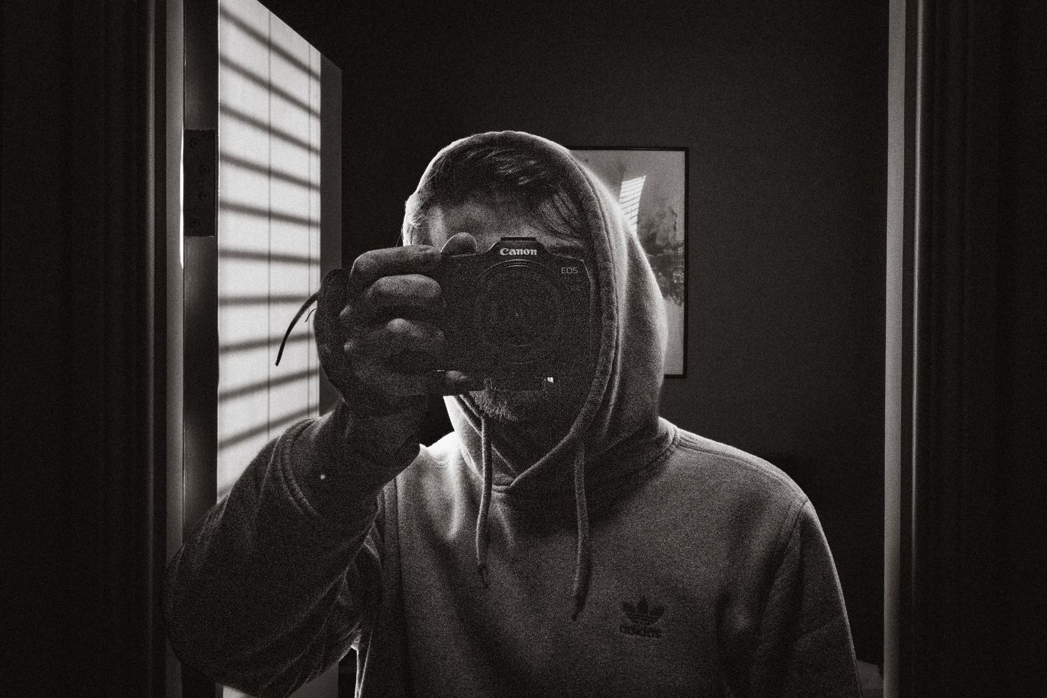 Person in hoodie taking mirror selfie with camera, black and white photography self-portrait.