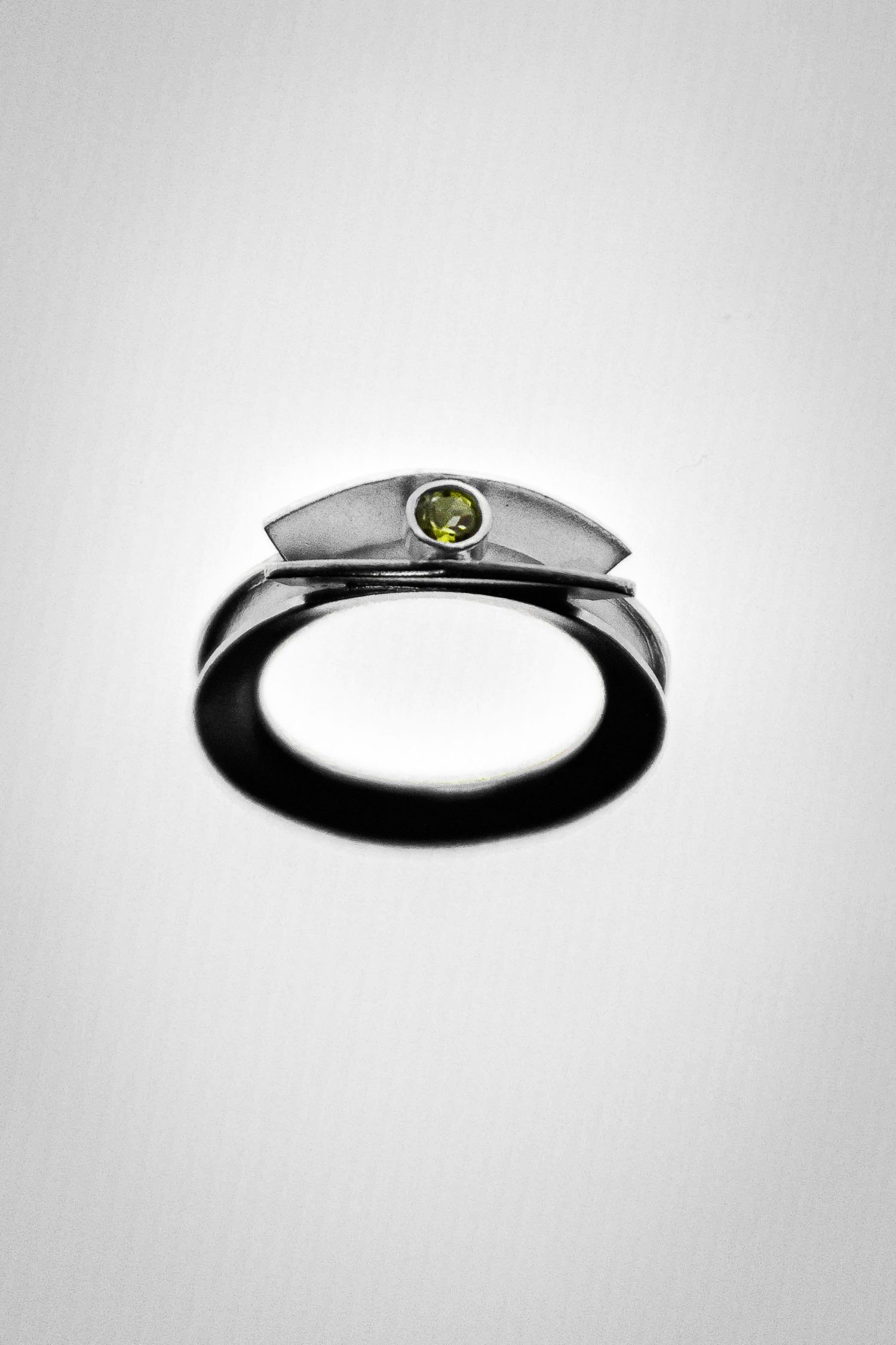 Silver ring with a geometric setting featuring a round green peridot gemstone on a white background.