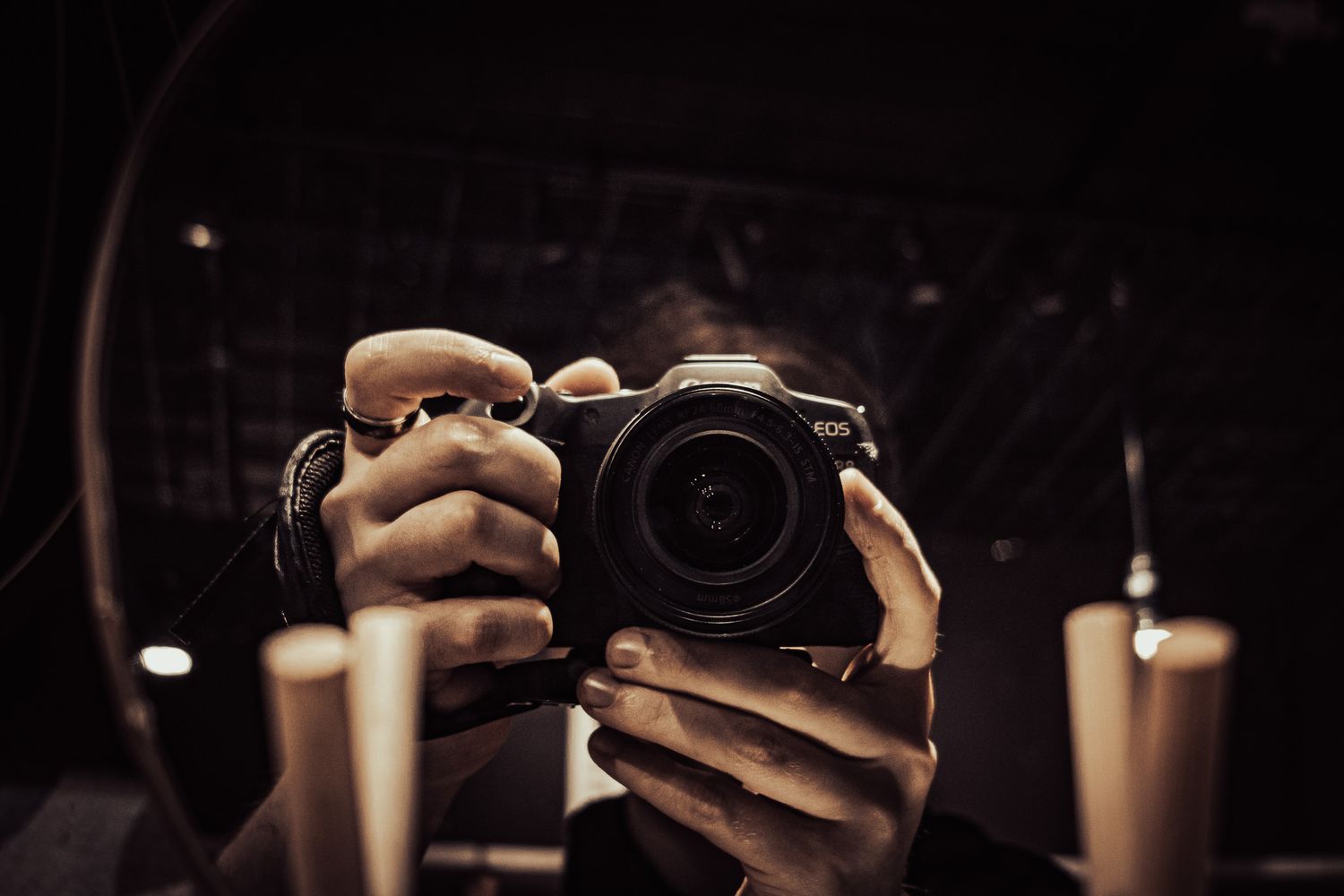 Photographer capturing a mirror selfie holding a Canon EOS camera in a dimly lit room.