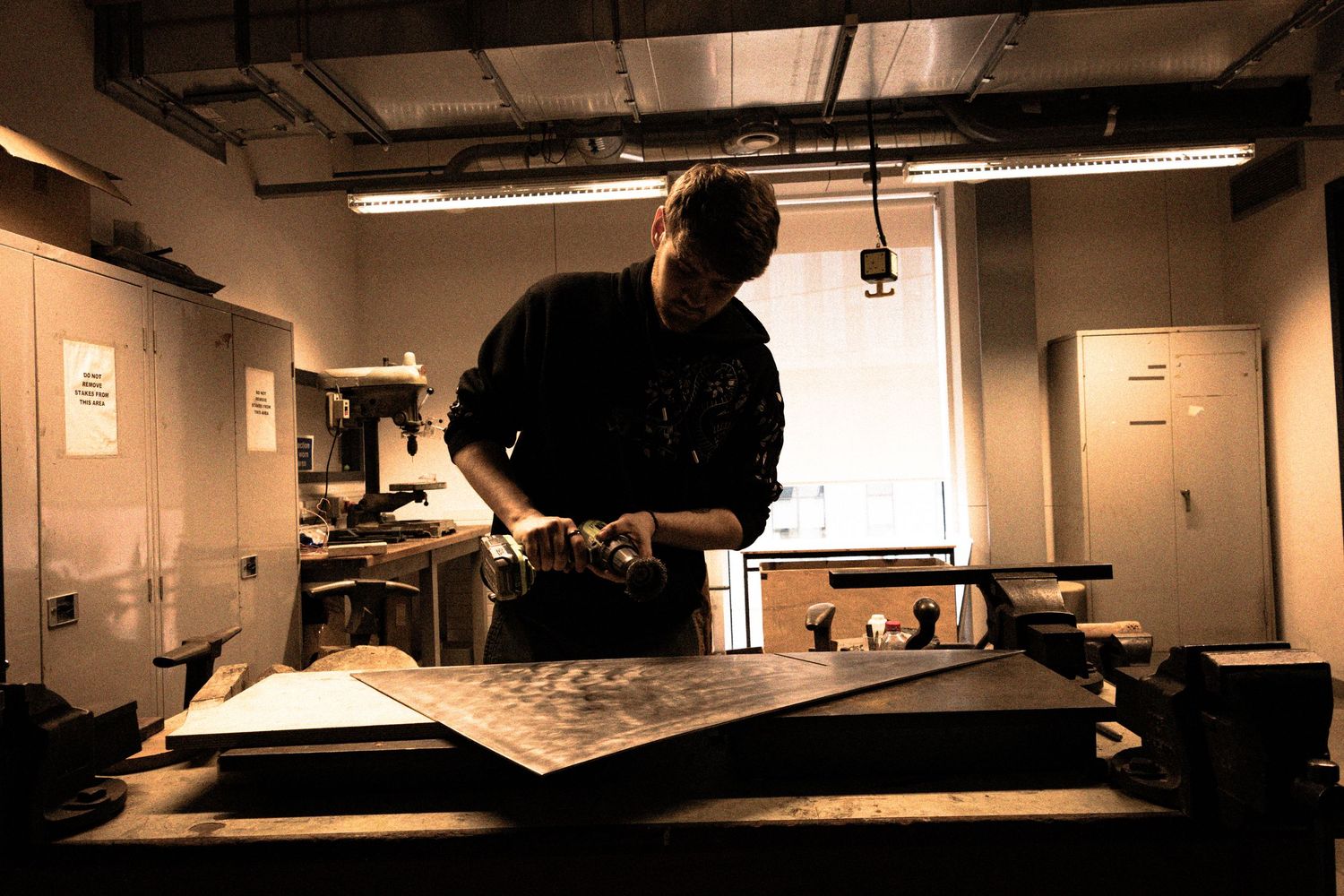 A craftsman works under bright lights in a dimly lit workshop, focused on a large flat surface with tools nearby.