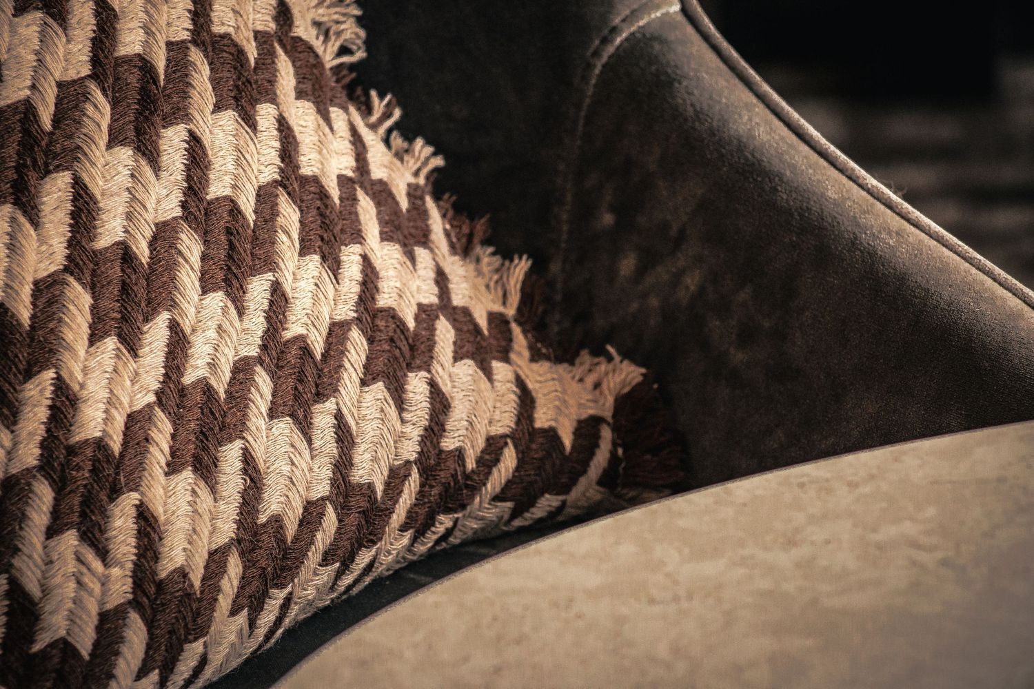 Close-up of a brown and beige houndstooth patterned cushion on a dark velvet chair.