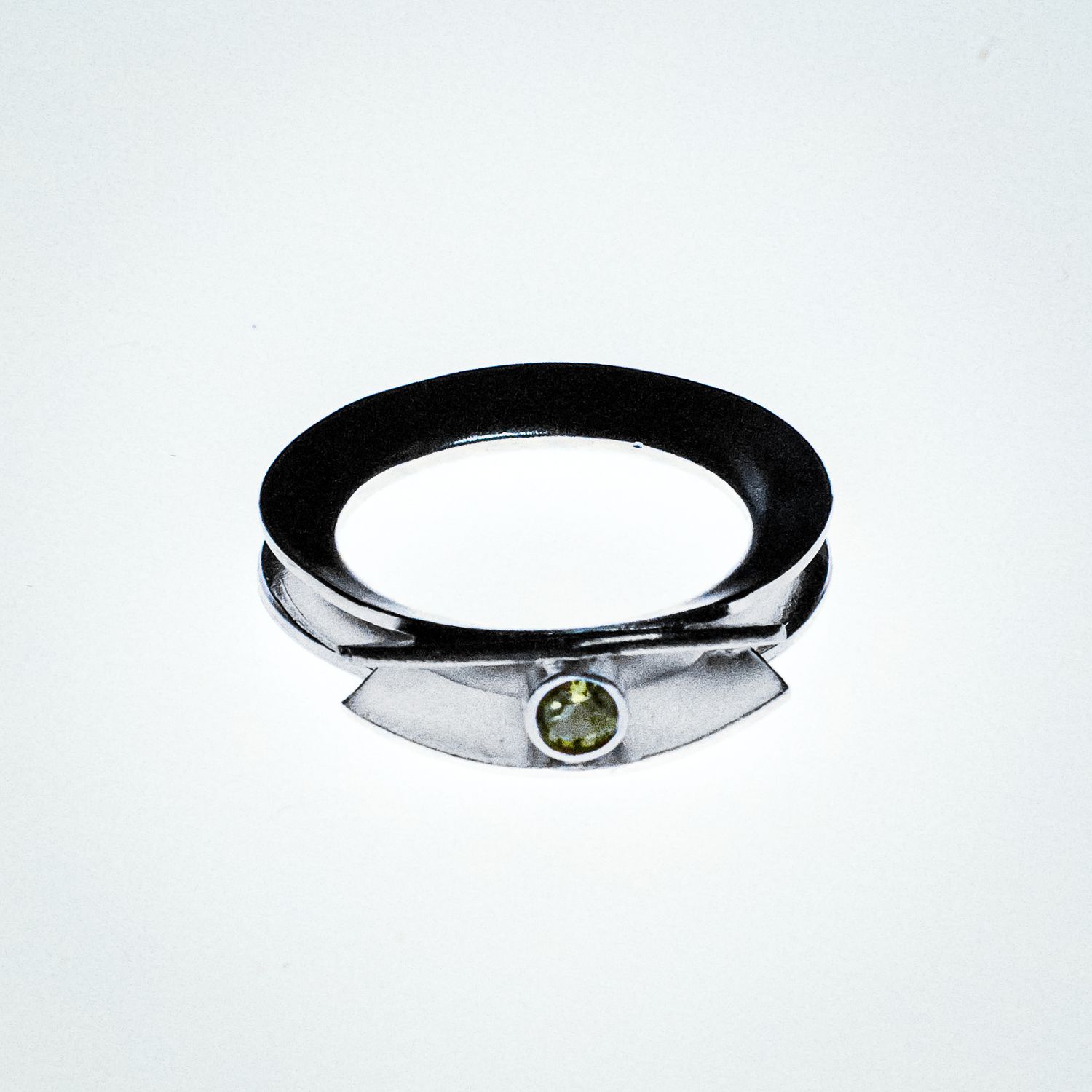 A modern silver ring with a small green peridot gemstone set in a unique angular design.