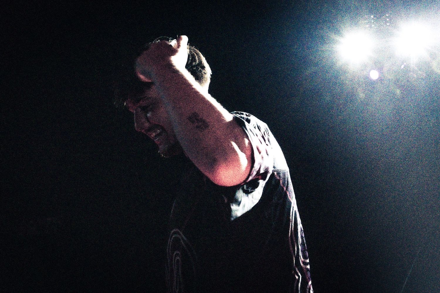 Performer on stage raising fist under bright spotlight in dark concert venue.