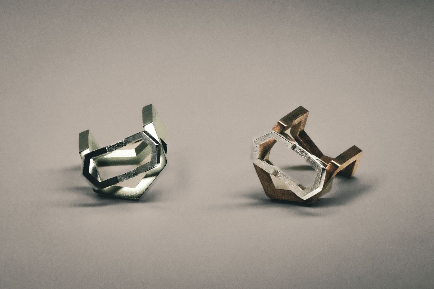 Two geometric silver rings with hexagonal design displayed on a grey surface.