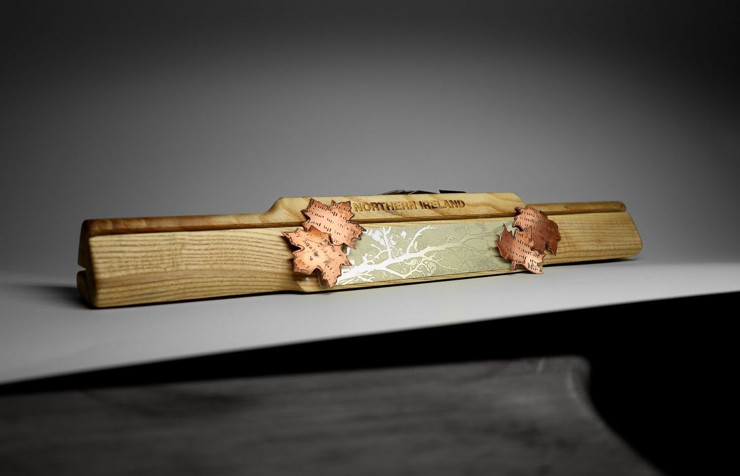 Vintage wooden tie clip with decorative copper leaf motifs and floral engraving on green enamel centerpiece.