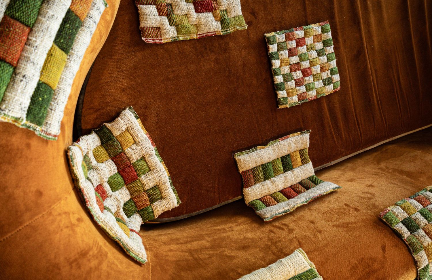 Colorful woven patchwork quilted coasters and placemats arranged on a warm brown wooden surface.