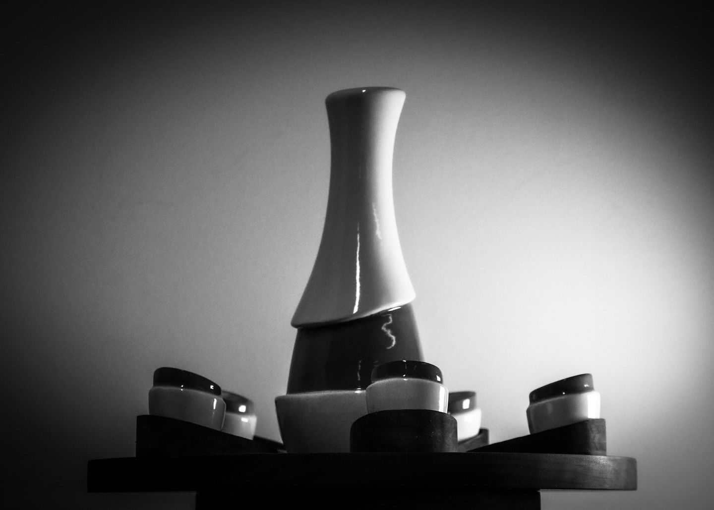 Black and white photo of an elegant white ceramic vase surrounded by small bowls on a platform.