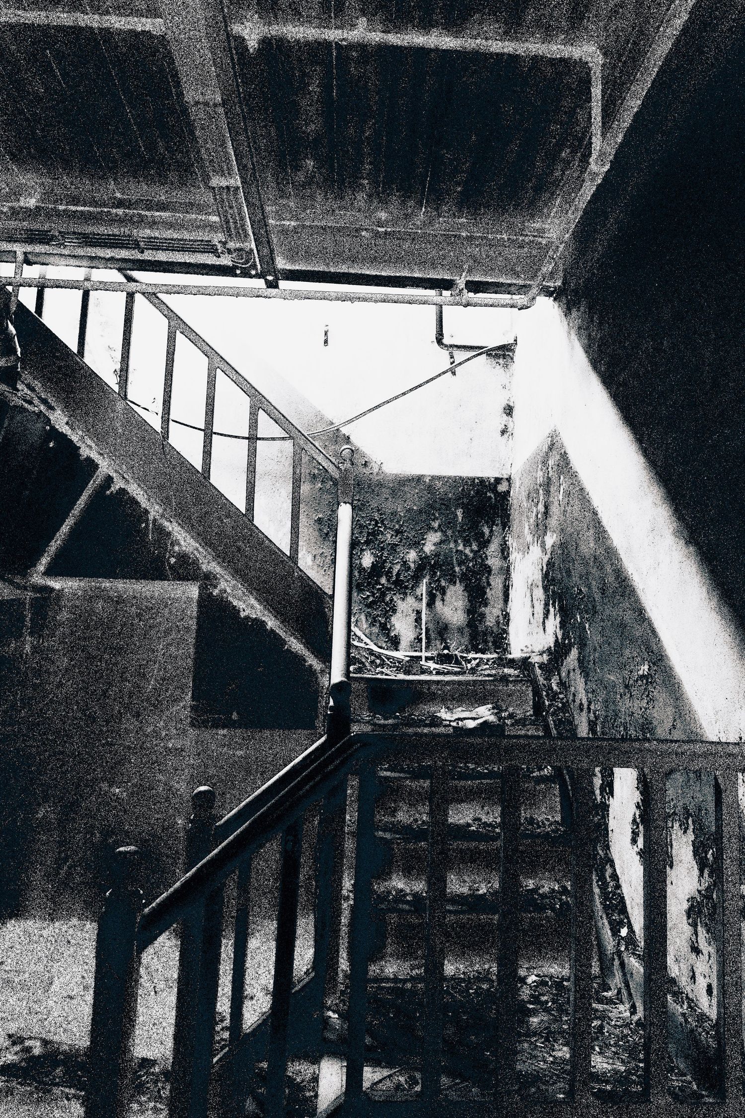 Black and white photo of a decayed, abandoned building interior with rusty metal stairs and deteriorating walls.