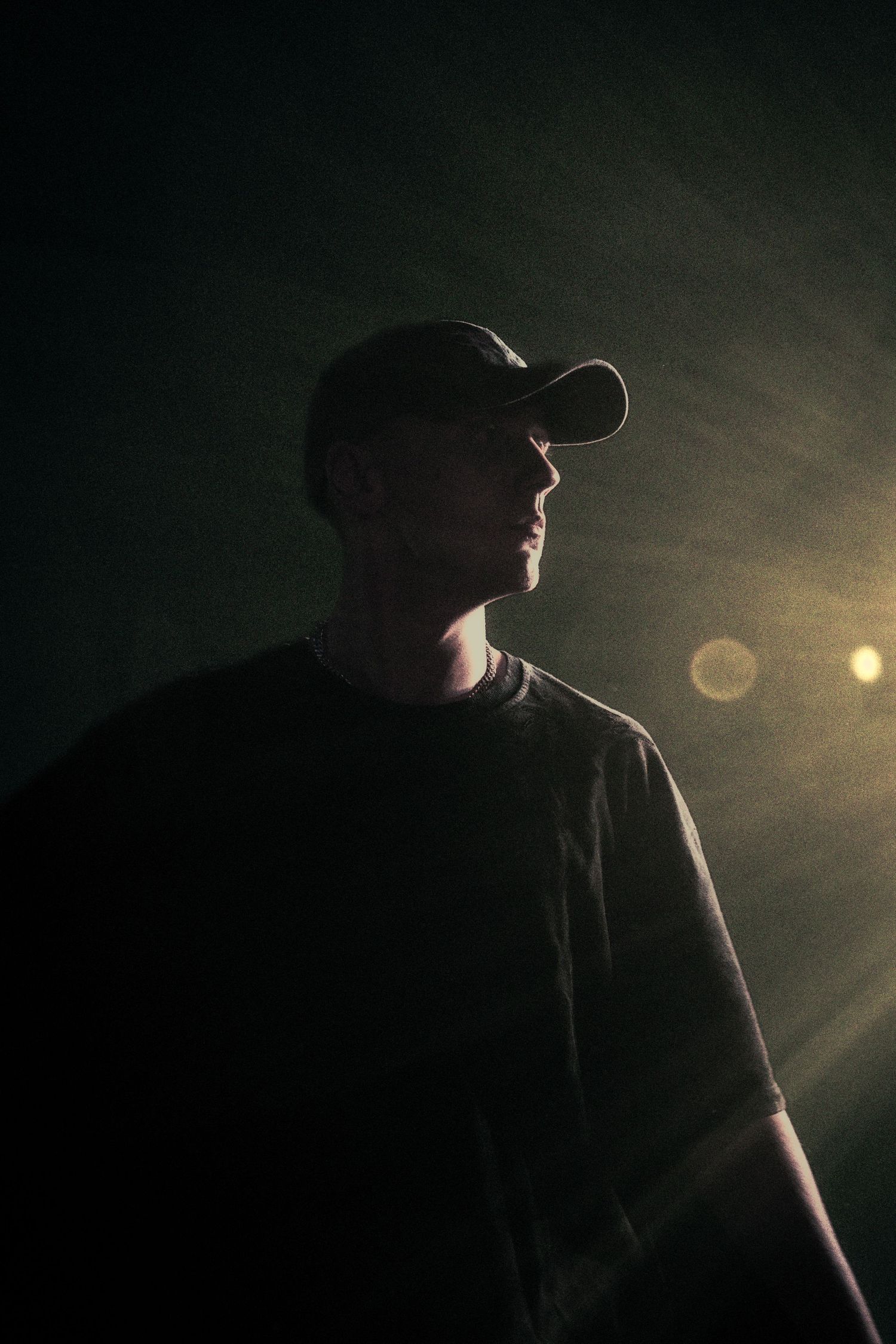 Silhouetted man in cap and t-shirt standing in dramatic dark green light with bokeh lens flare effect.