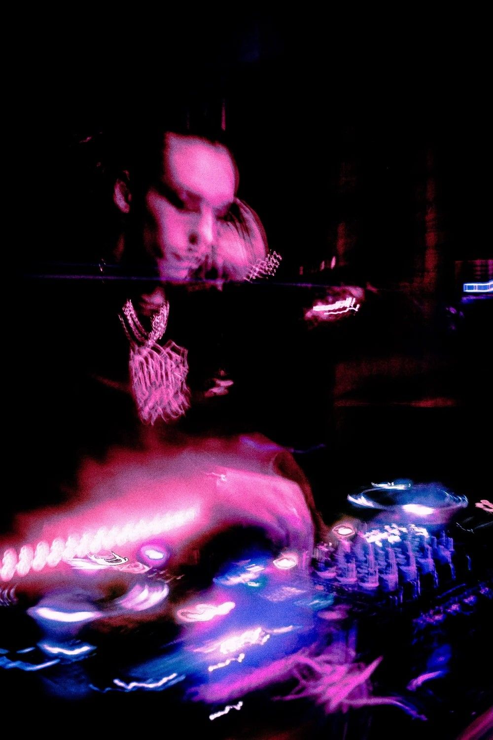DJ performing at a nightclub with colorful pink and blue neon lights illuminating the mixing equipment.