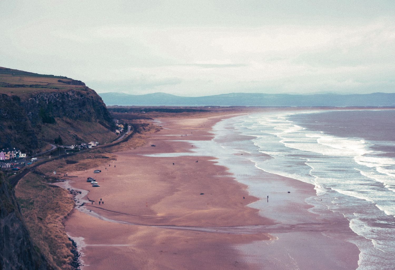 Aerial view of a wide sandy beach with gentle waves and coastal cliffs.