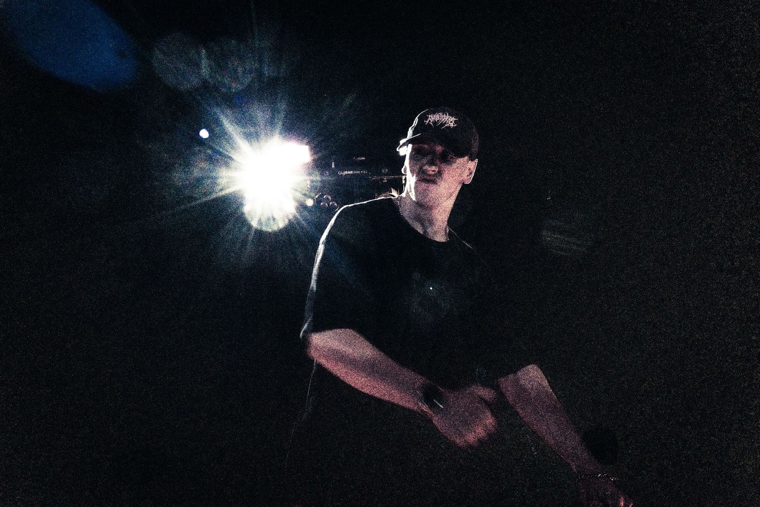 Man in black t-shirt and cap illuminated by bright light against dark background at night.