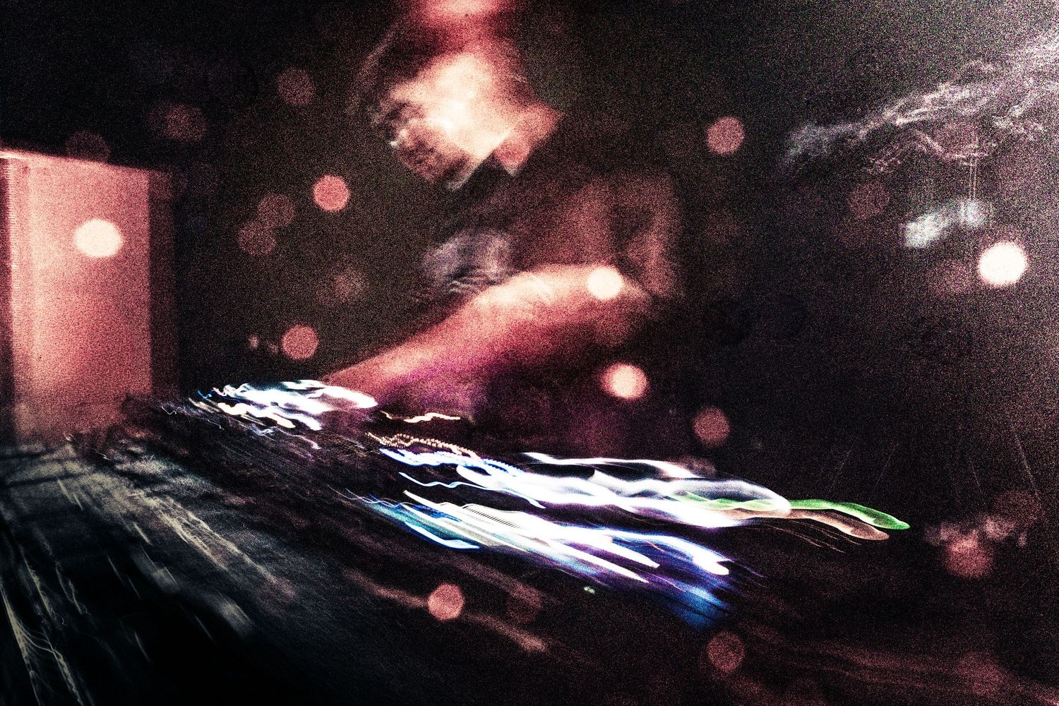 DJ performing at a dark concert venue with colorful light streaks on turntables and bokeh effects.