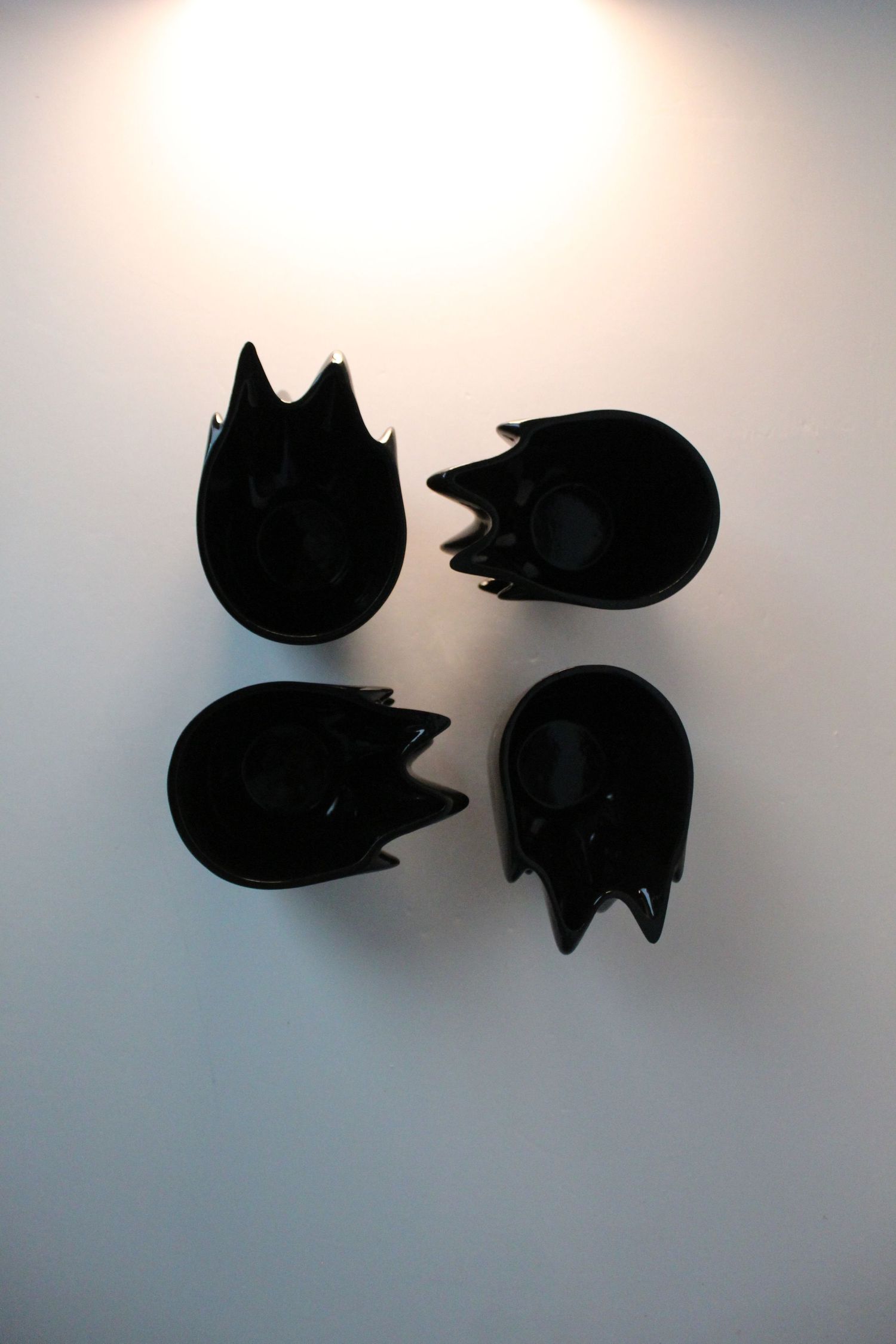Four black ceramic bowls with jagged edges arranged in a grid on a white surface.