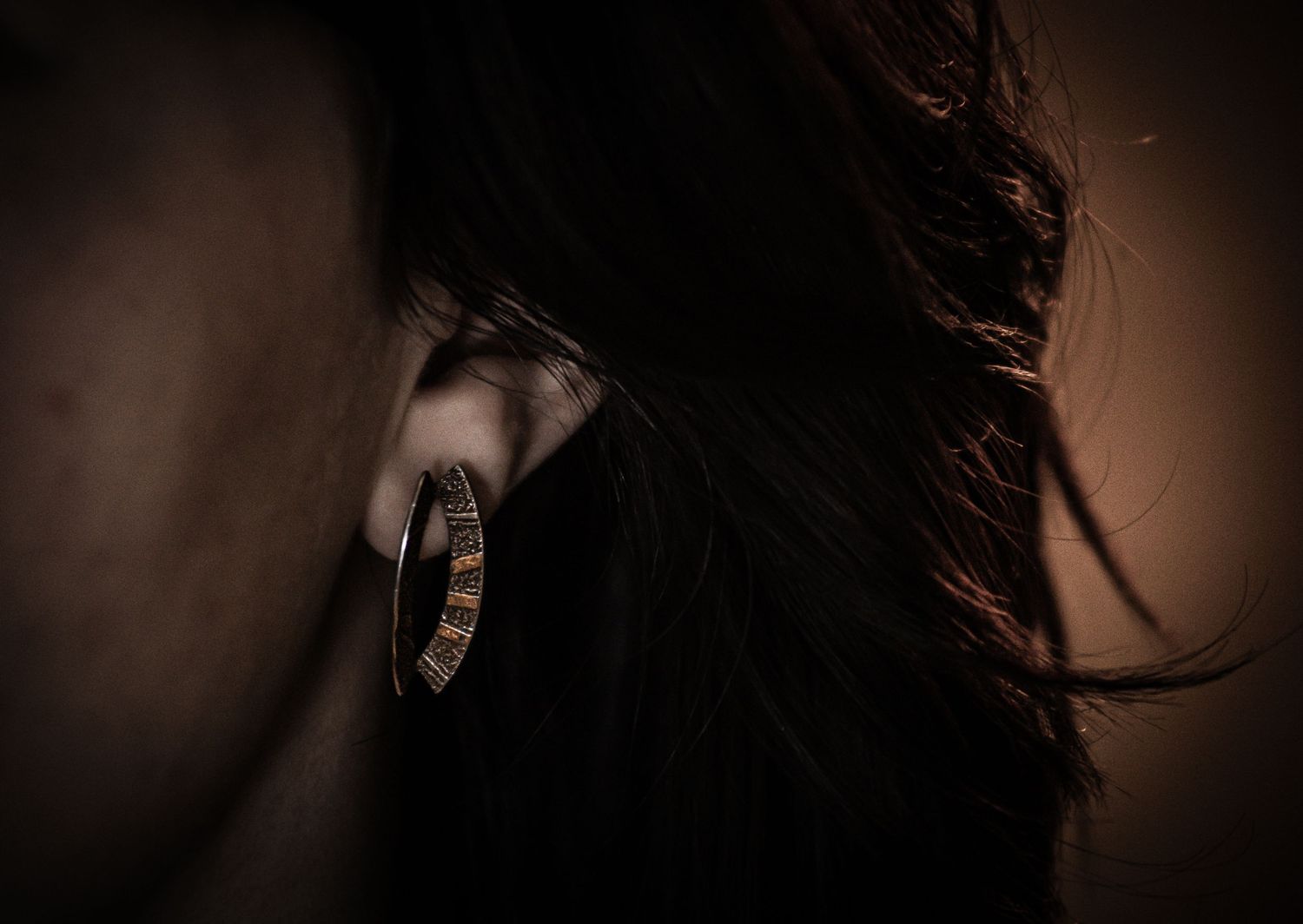 Close-up of a woman wearing a gold hoop earring with dark hair falling over her shoulder.