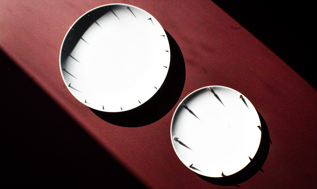Two minimalist white clock faces mounted on a dark red surface, casting dramatic shadows in moody lighting.