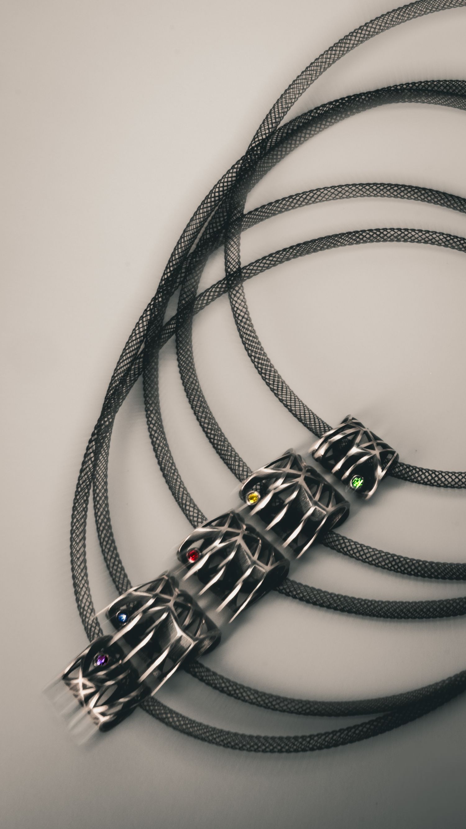 Dark metallic braided audio cable with ornate silver connectors featuring colorful gemstone accents on a light gray background.