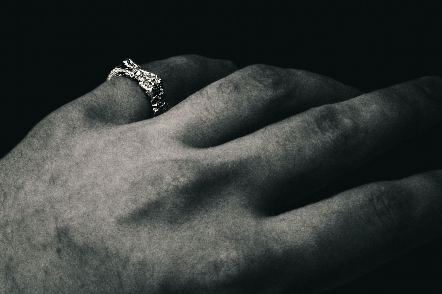 Close-up black and white photo of a hand wearing an ornate silver ring with intricate detailing.