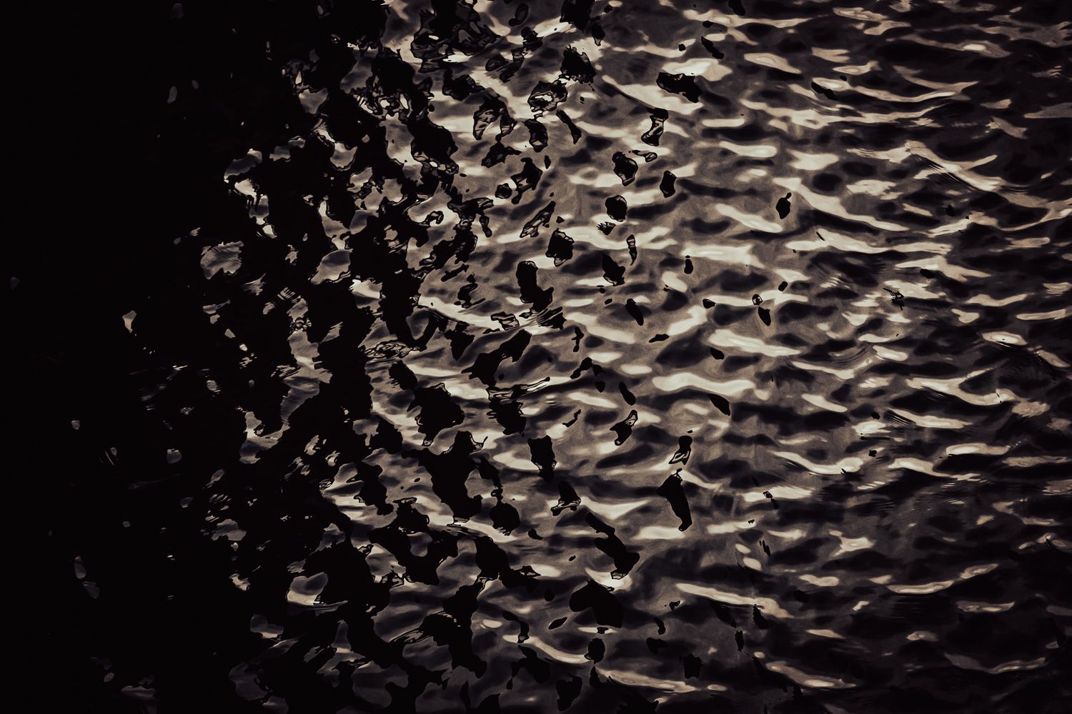 Close-up of dark, rippling wet sand texture with dramatic light reflections creating an abstract pattern.