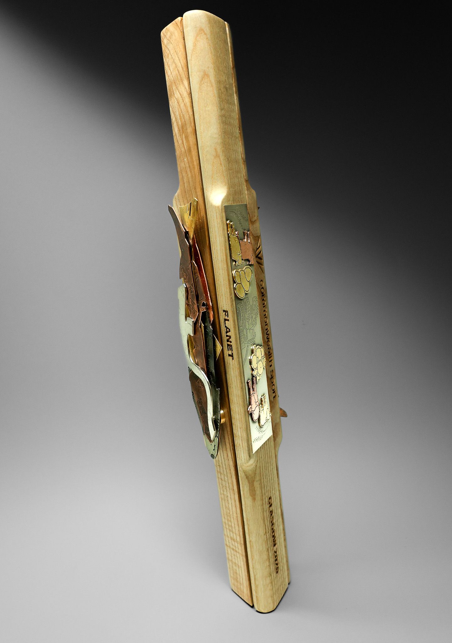Gold and wood decorative firearm displayed vertically, showcasing intricate metalwork and engravings on a gray background.