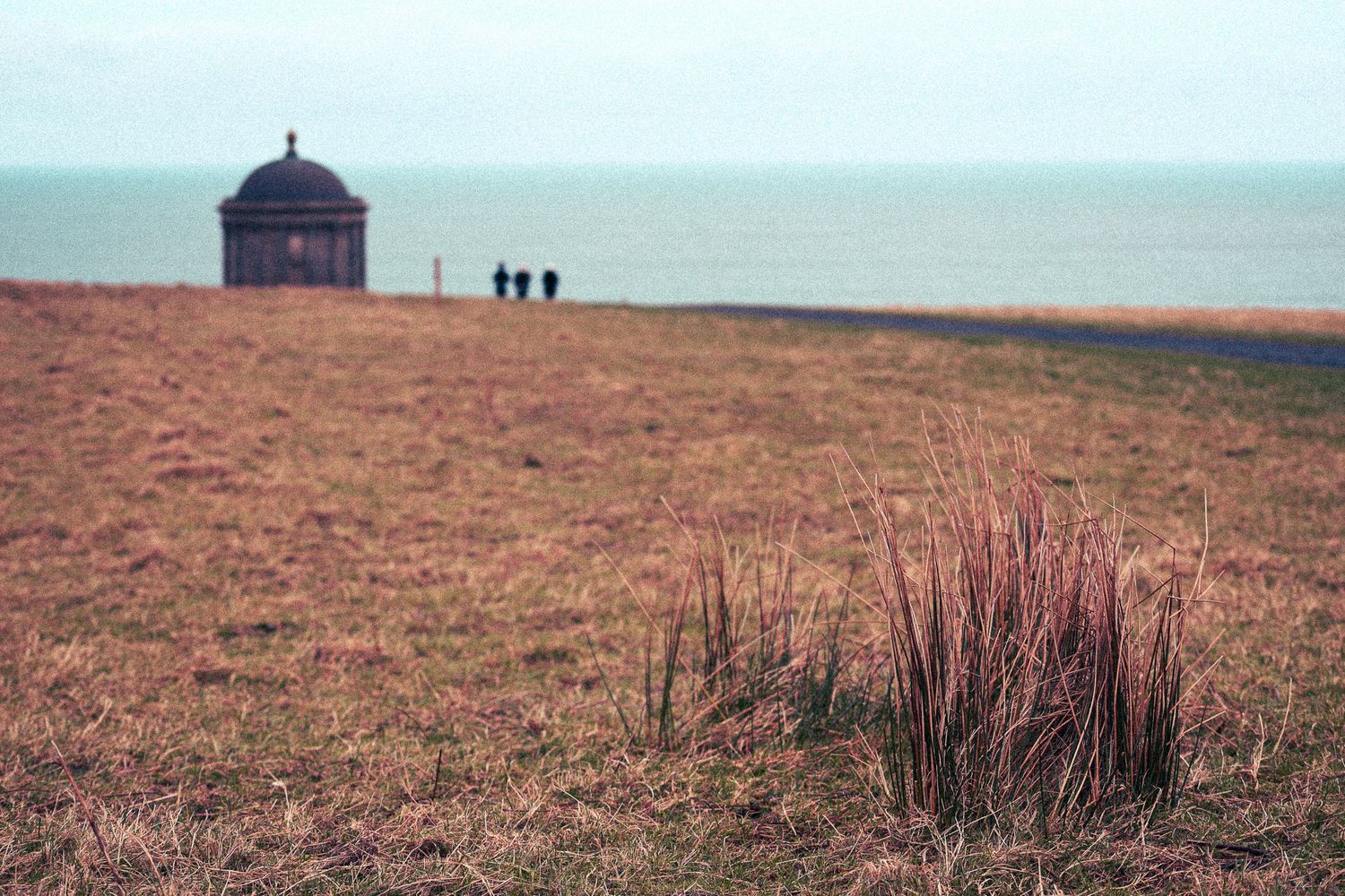 Mussenden Temple on clifftop overlooking the sea with two distant figures nearby.
