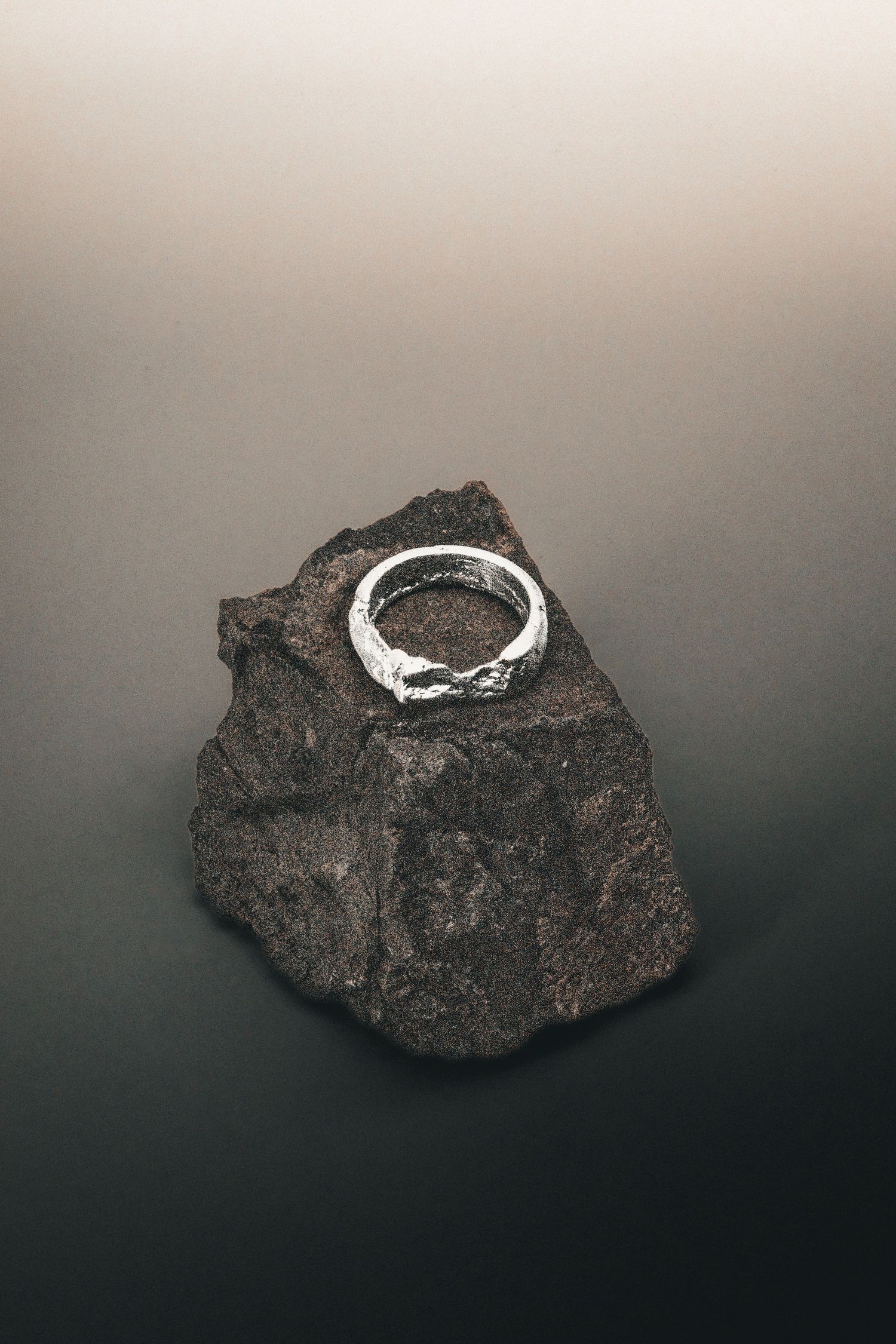 Textured silver ring resting on a dark volcanic rock against a gradient gray background.
