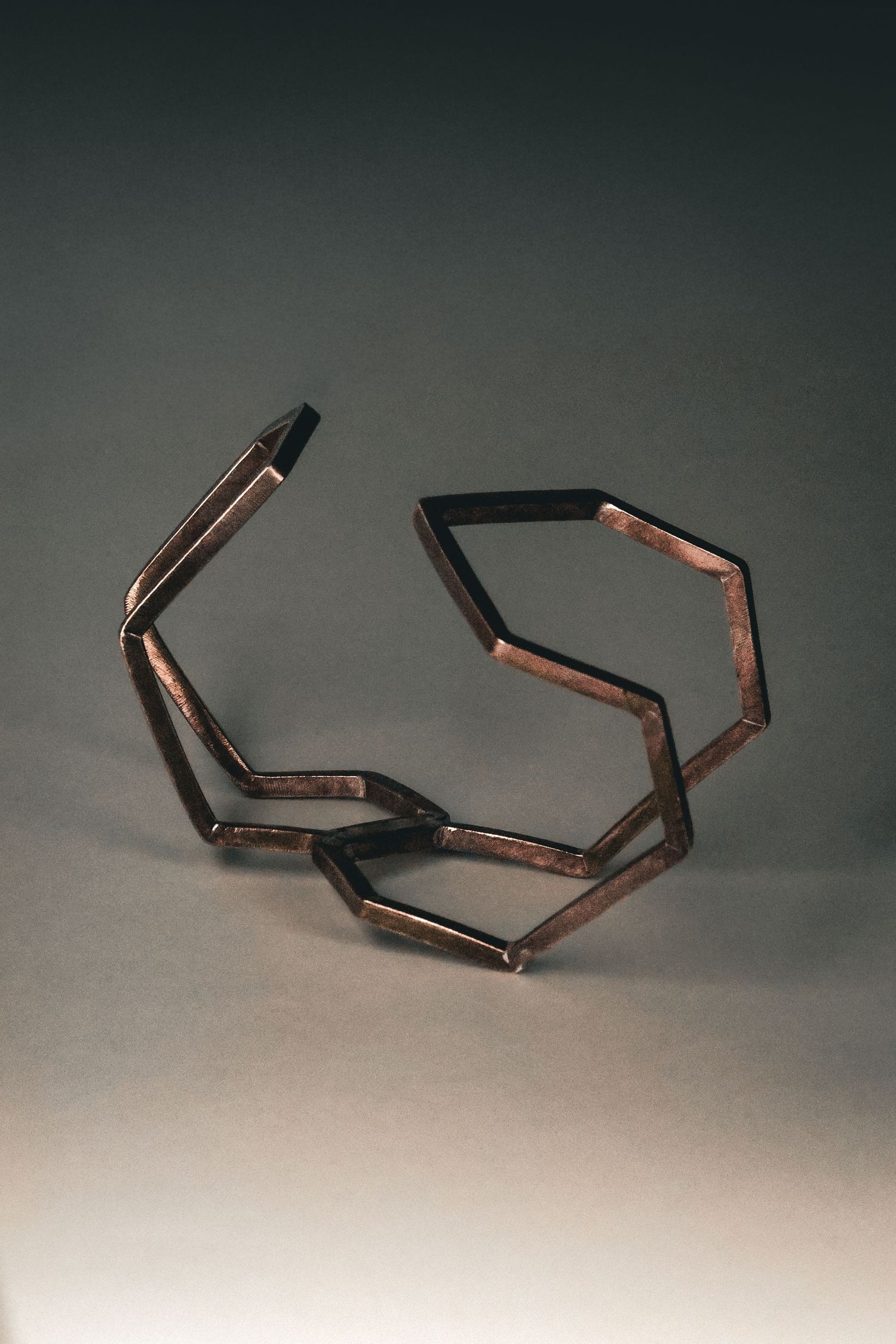 Geometric copper cuff bracelet with linked hexagonal shapes on a grey background.