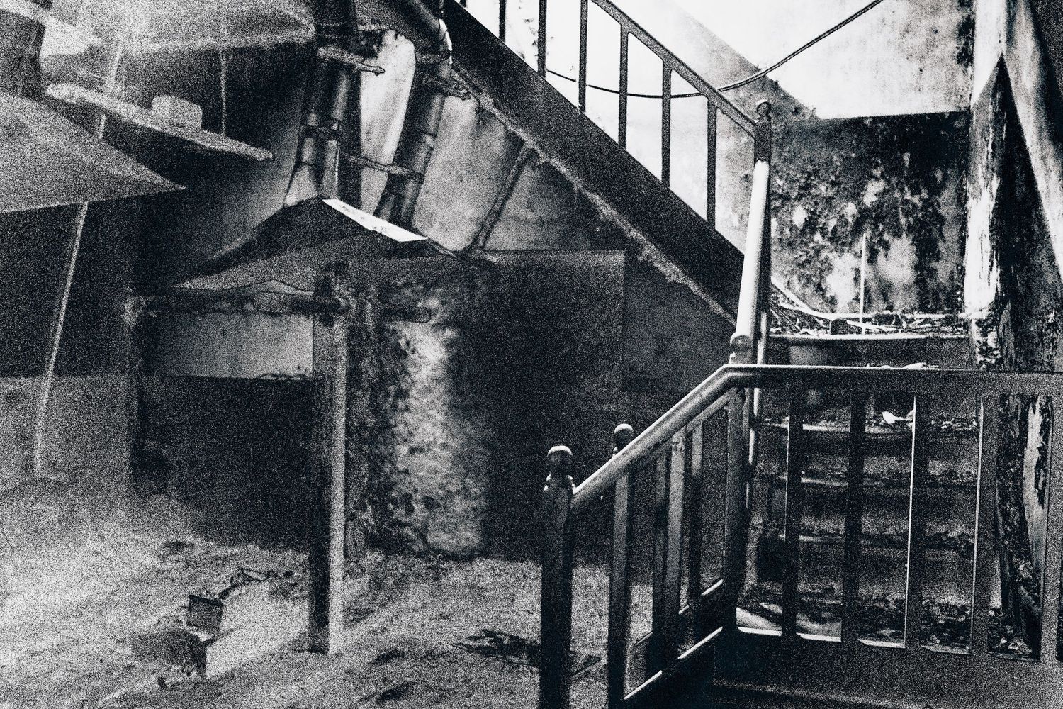 Black and white photo of a fire-damaged interior staircase with charred walls and debris on the floor.