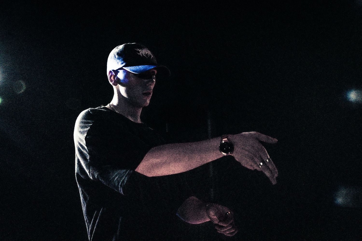 Man in black t-shirt and futuristic blue LED glasses pointing finger on dark stage.