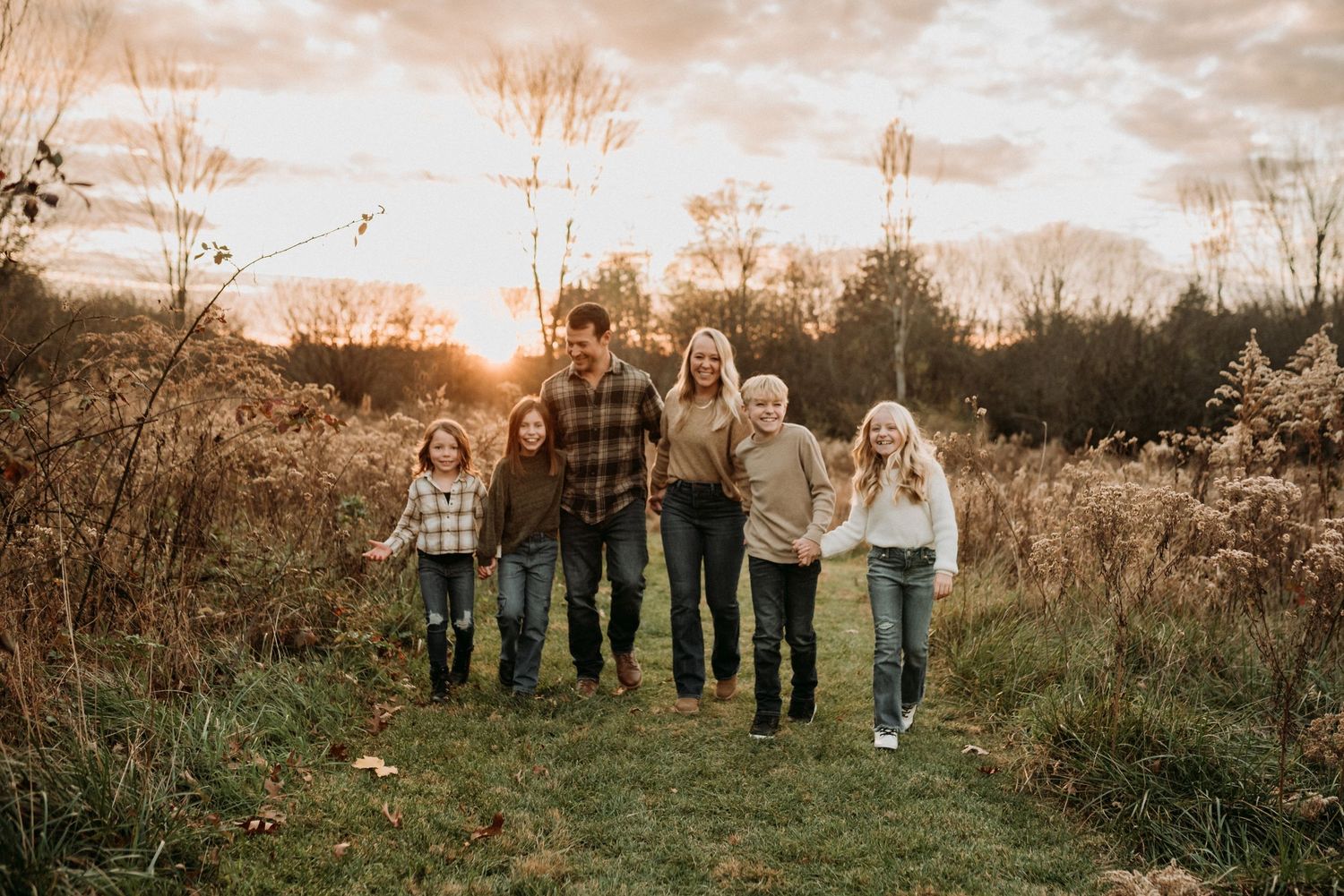 A joyful family of five walks together through a golden field at sunset.