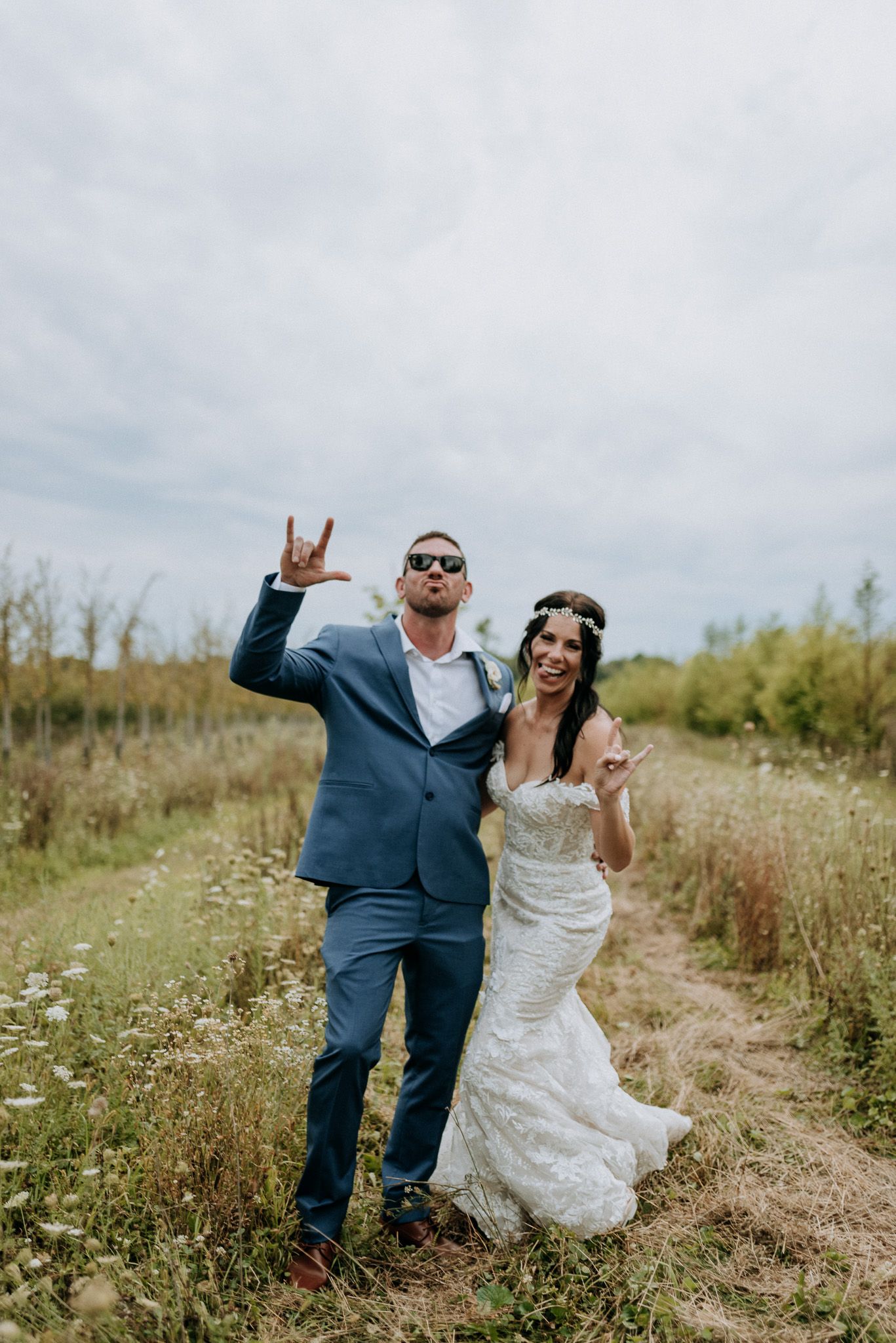 Bride and groom making rock signs in a wildflower field on their wedding day in casual fun pose.