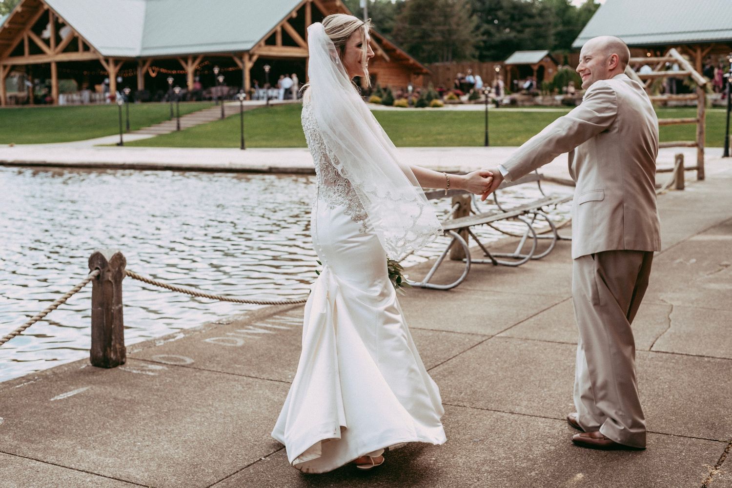 Bride and groom dancing by a lakeside venue, bride in flowing white gown with veil.